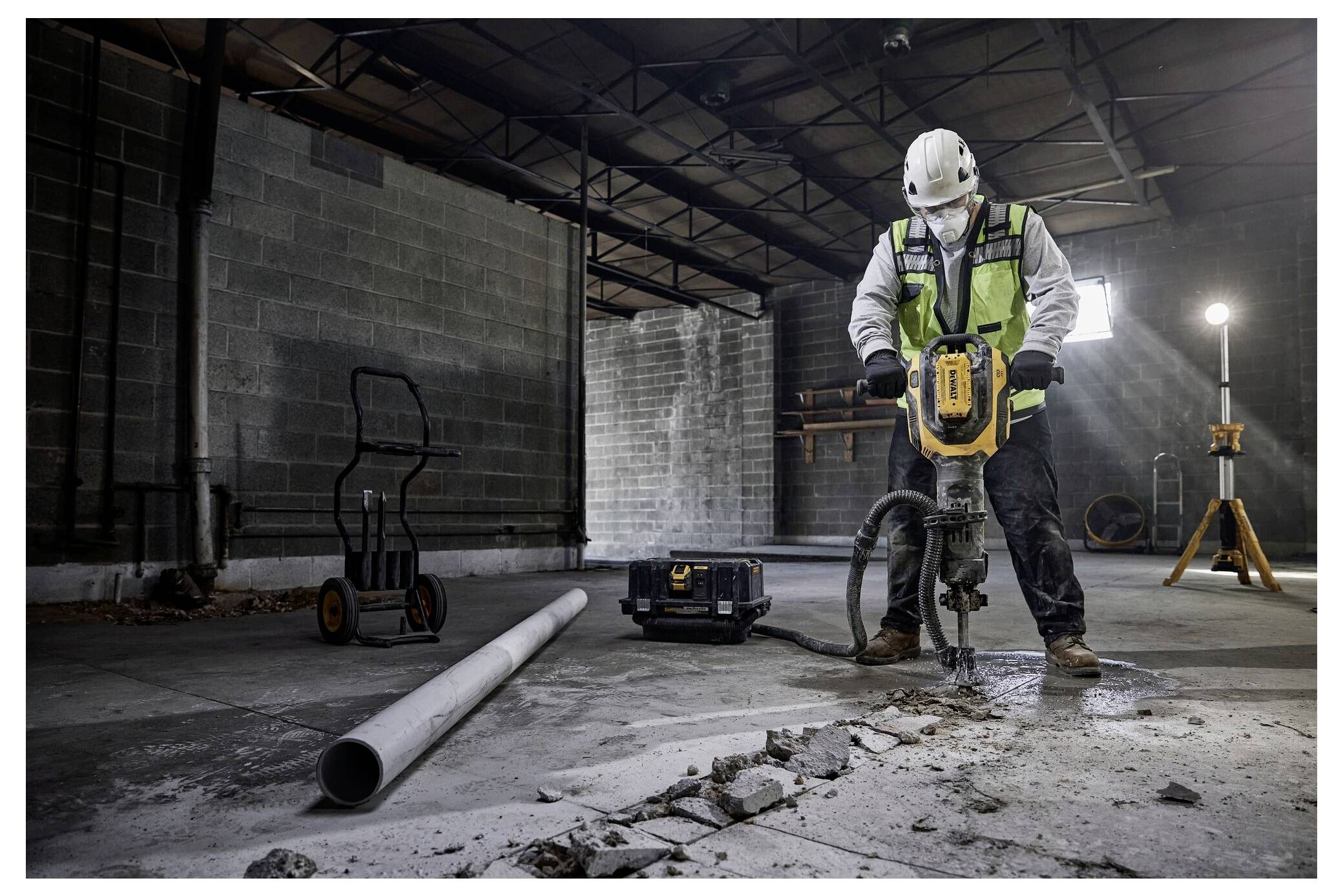 Ein Bauarbeiter mit Helm und Sicherheitsweste bedient einen Presslufthammer in einem unfertigen Gebäude, umgeben von Ausrüstung und Schutt.