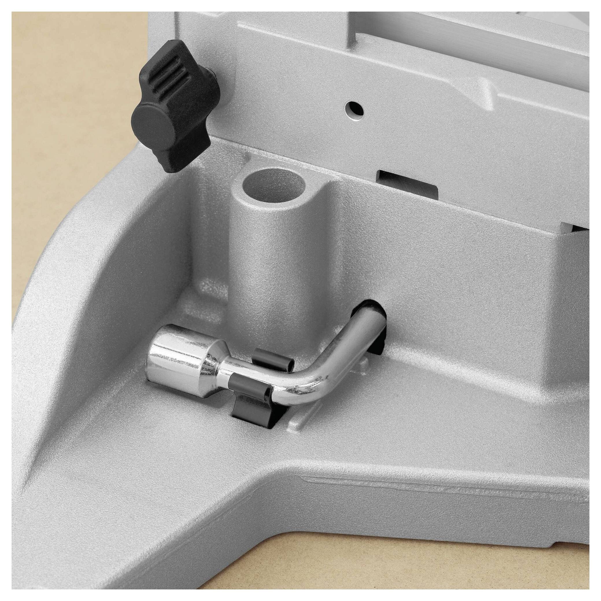 Eine Nahaufnahme einer metallischen Werkzeugkomponente mit einem Hebel und einem Einstellknopf auf einer beigen Oberfläche. Die Komponente deutet auf eine mechanische Einstellung hin.