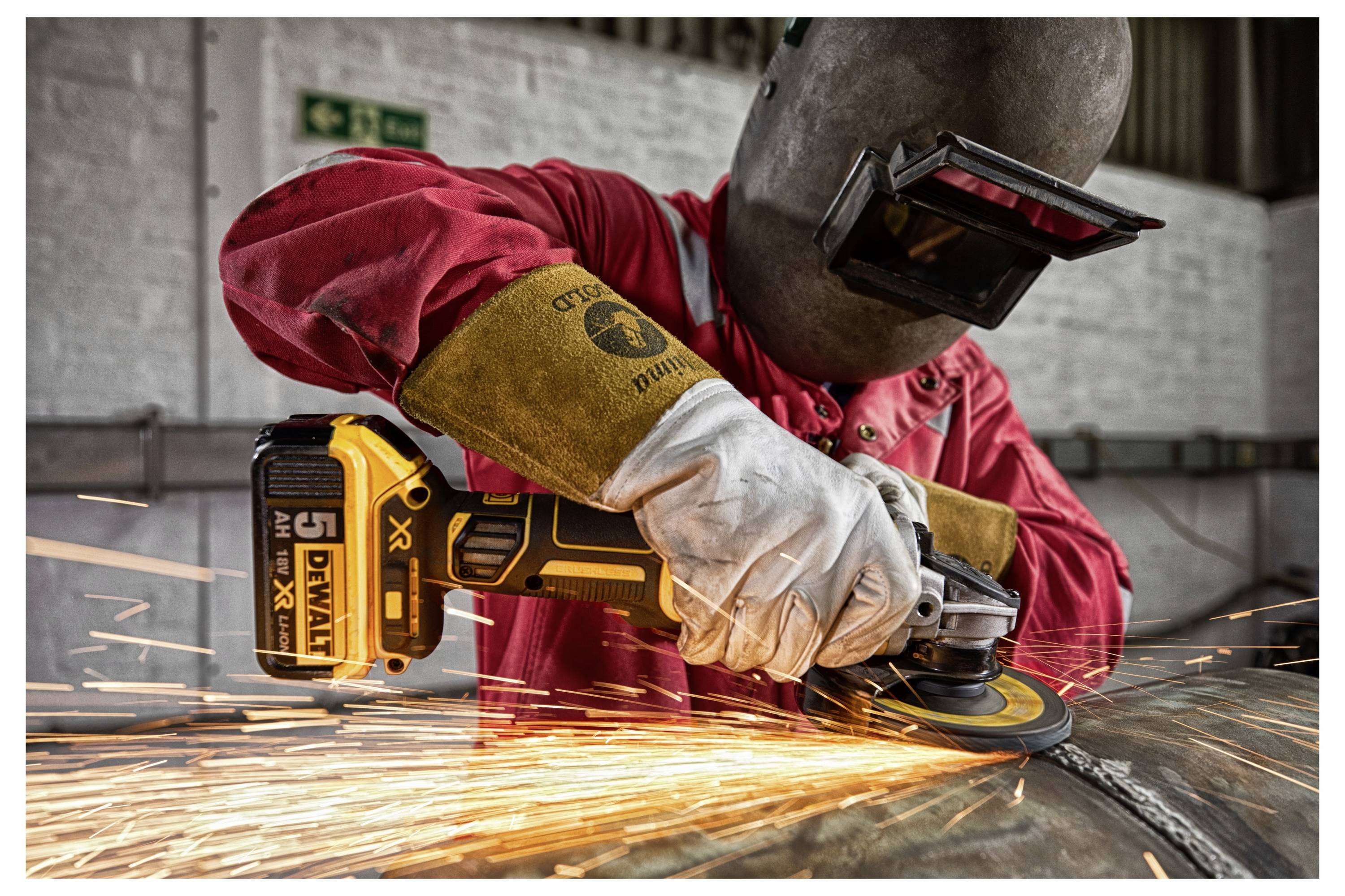 Eine Person in Schutzausrüstung, die einen Winkelschleifer benutzt, Funken fliegen vom Metall, was Industriearbeit und Sicherheitsvorkehrungen zeigt.