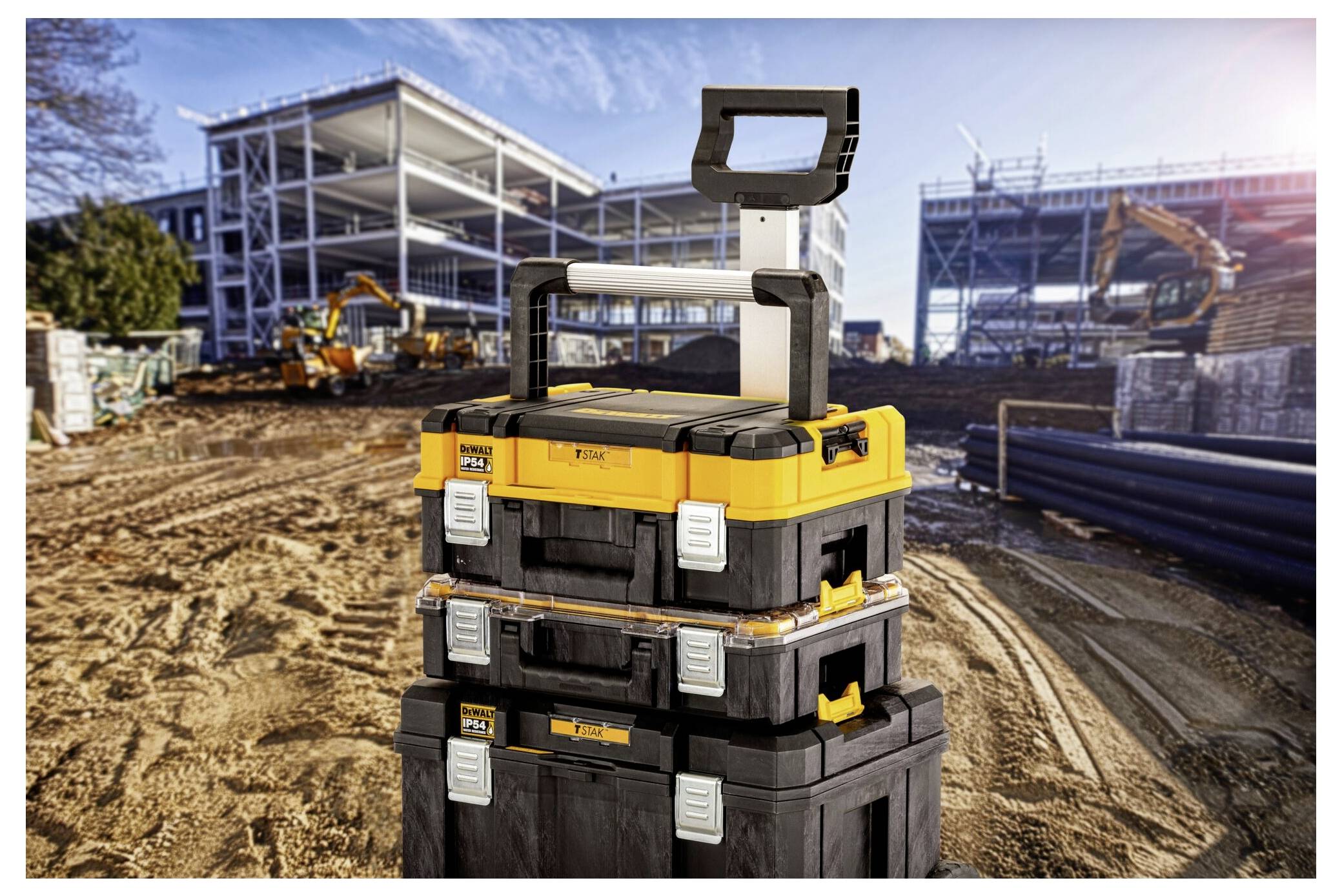 Gestapelte Werkzeugkästen mit einem Griff, auf einer Baustelle mit Gebäuden und Maschinen im Hintergrund.