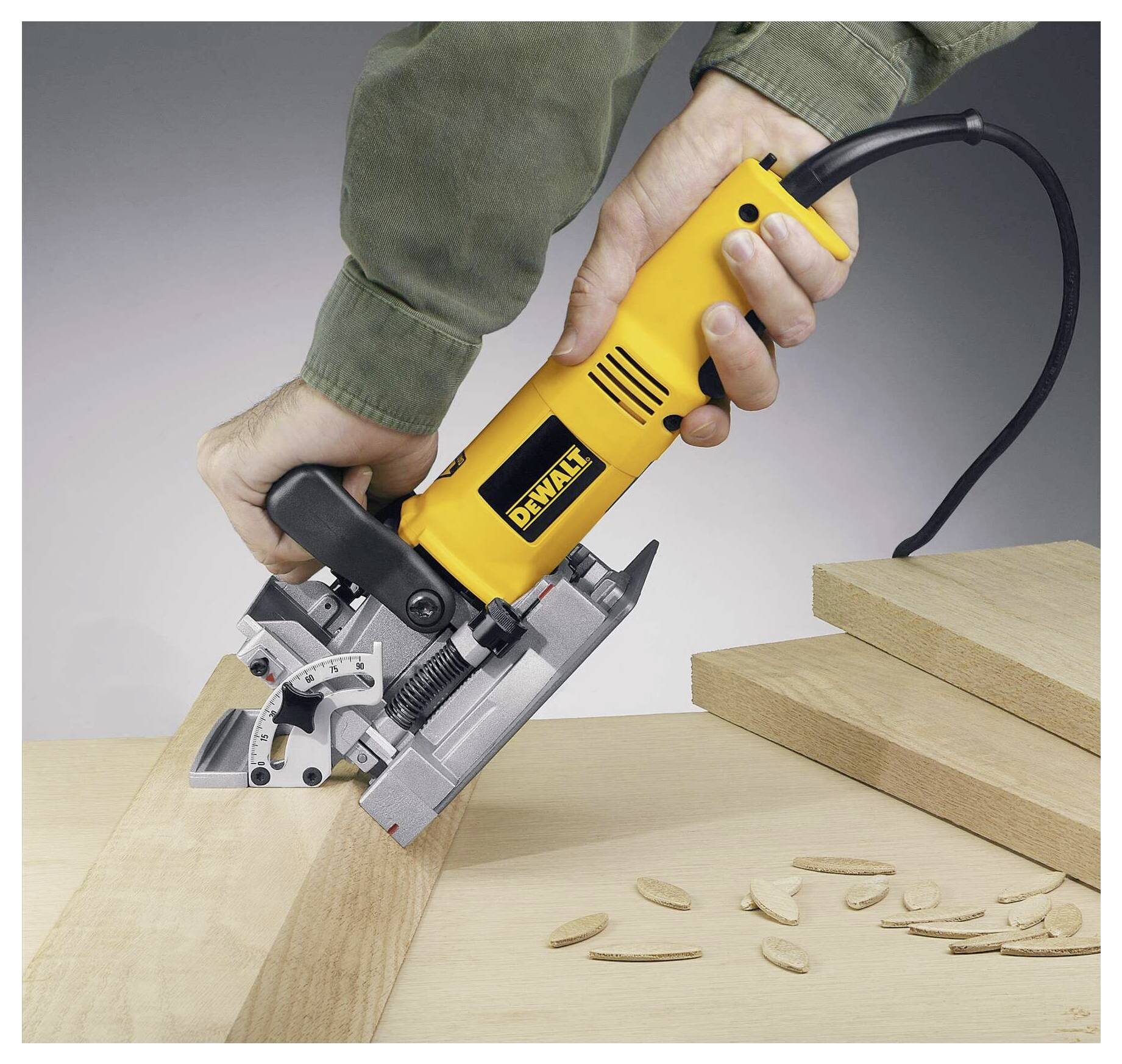 Eine Person verwendet ein gelbes Keksdübel-Werkzeug, um Schlitze in Holzbretter zu schneiden, mit mehreren kleinen Holzkeksdübeln in der Nähe verstreut.