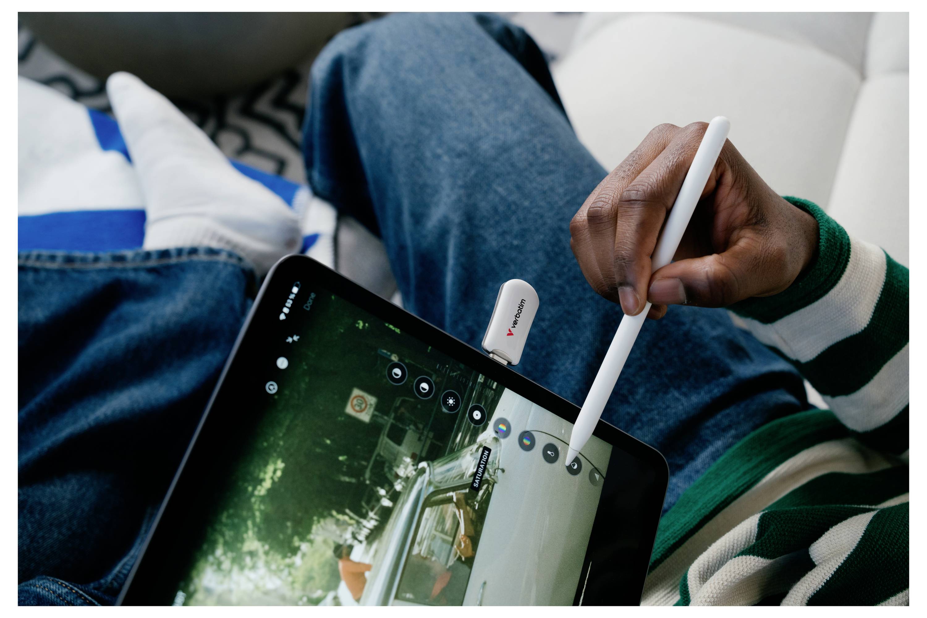 Eine Person nutzt einen weißen Stylus auf einem Tablet und zeichnet auf dem Bildschirm, während sie auf einem Sofa sitzt.