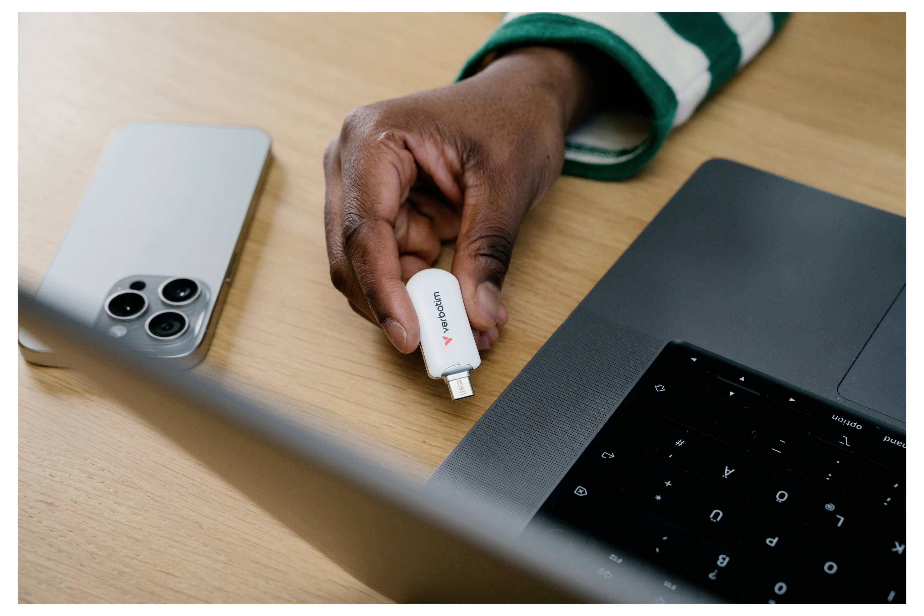 Hand steckt einen kleinen Lenovo USB-C-Adapter in einen Laptop neben einem Smartphone auf einem Holzschreibtisch.