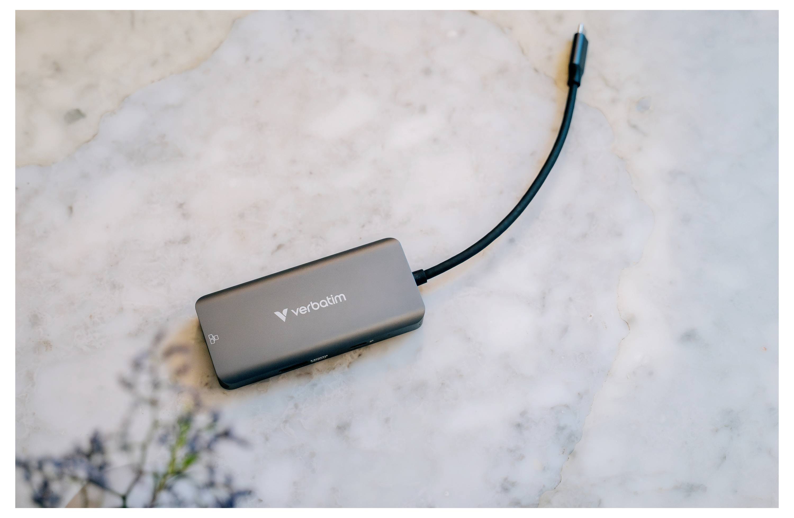 Ein schwarzer Verbatim USB-C-Hub mit angeschlossenem Kabel liegt auf einer hellen Marmoroberfläche.