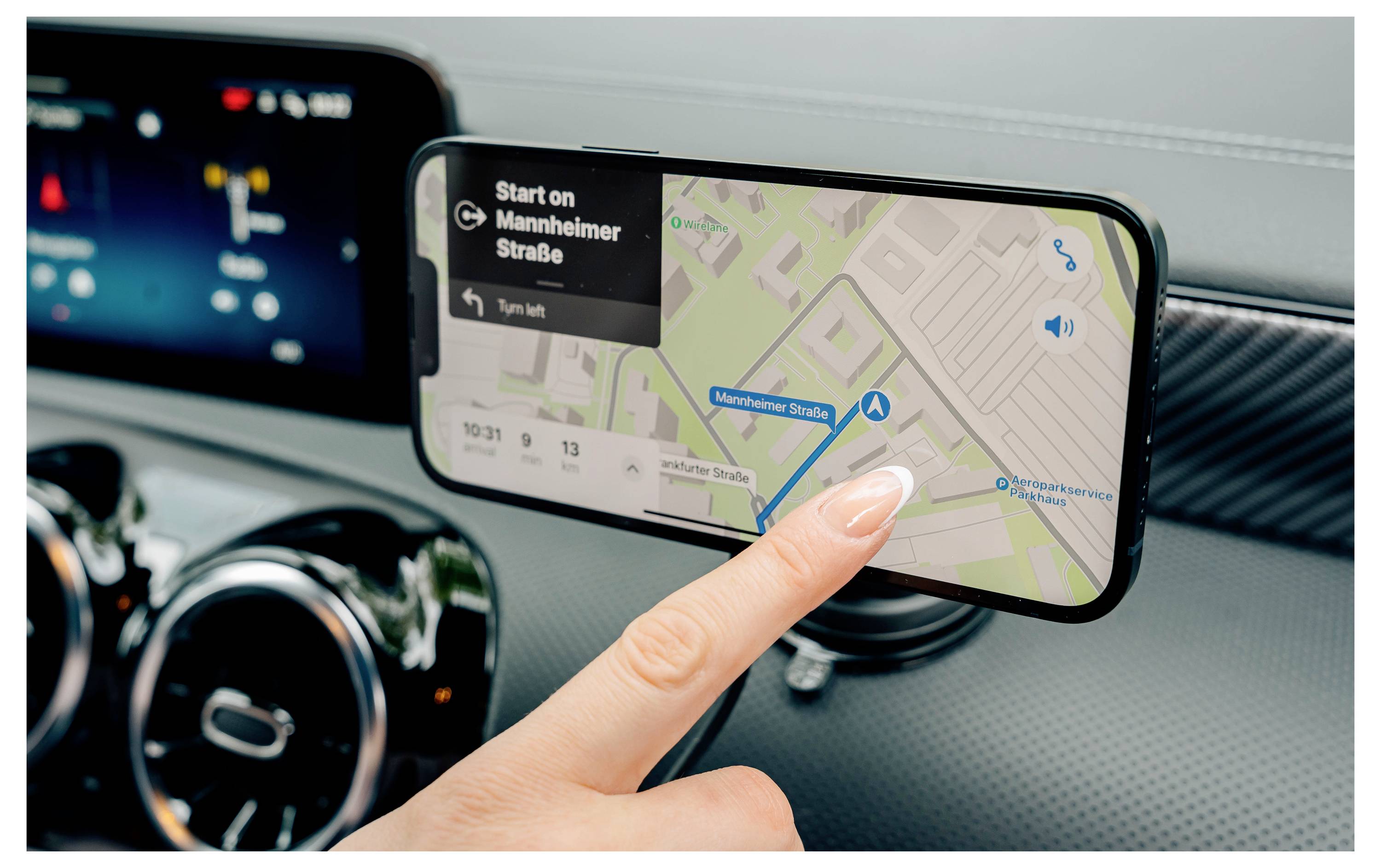 Eine Person nutzt ein Smartphone, das auf einer Armaturenbrett-Halterung befestigt ist, zur Navigation. Das Gerät zeigt eine Karte mit Schritt-für-Schritt-Anweisungen zur Mannheimstraße an.