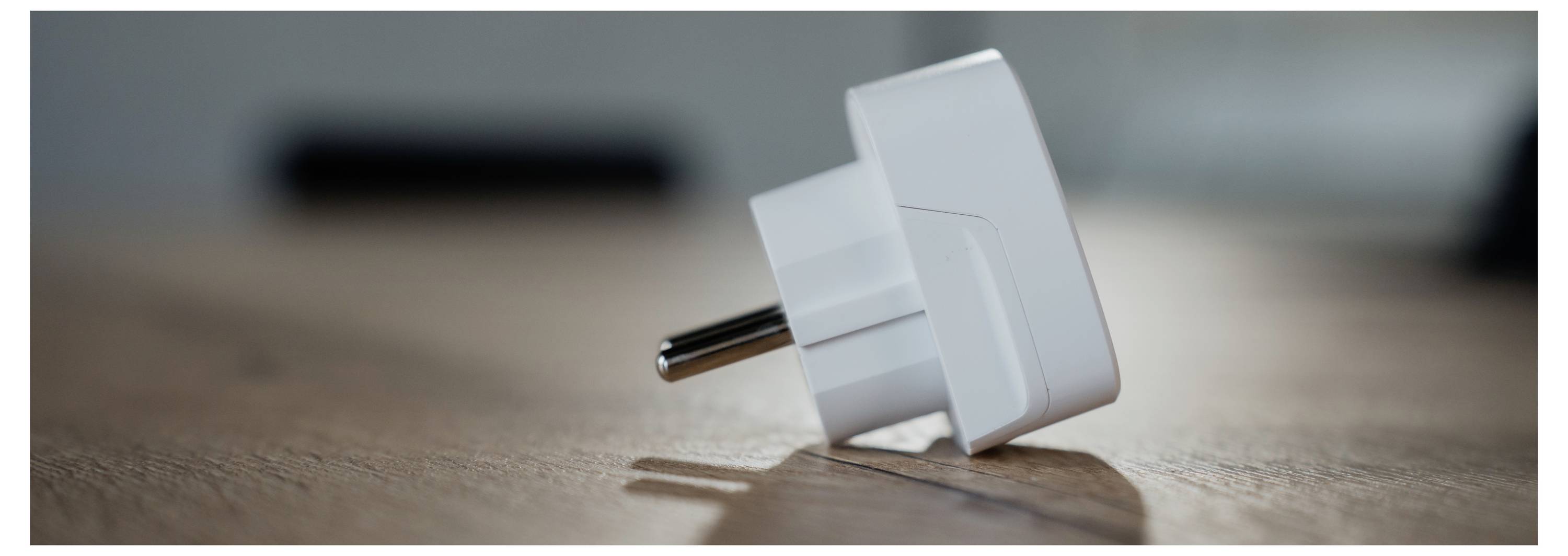 Ein weißer elektrischer Steckdosenadapter liegt auf einer Holzoberfläche, mit einem unscharfen Hintergrund.