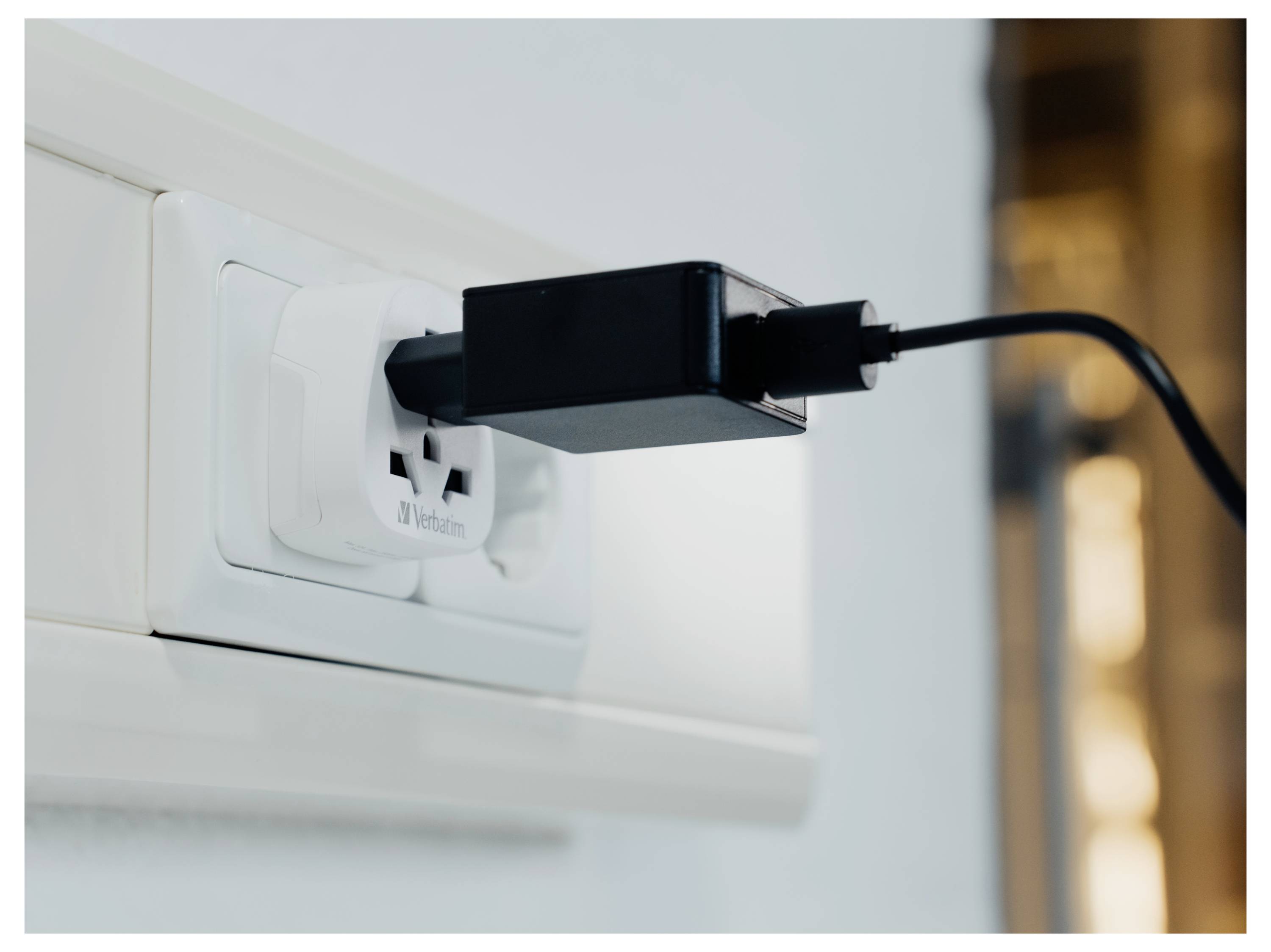 Schwarzer Stromanschlussadapter in eine weiße Wandsteckdose eingesteckt mit einem Kabel, das sich nach rechts erstreckt.