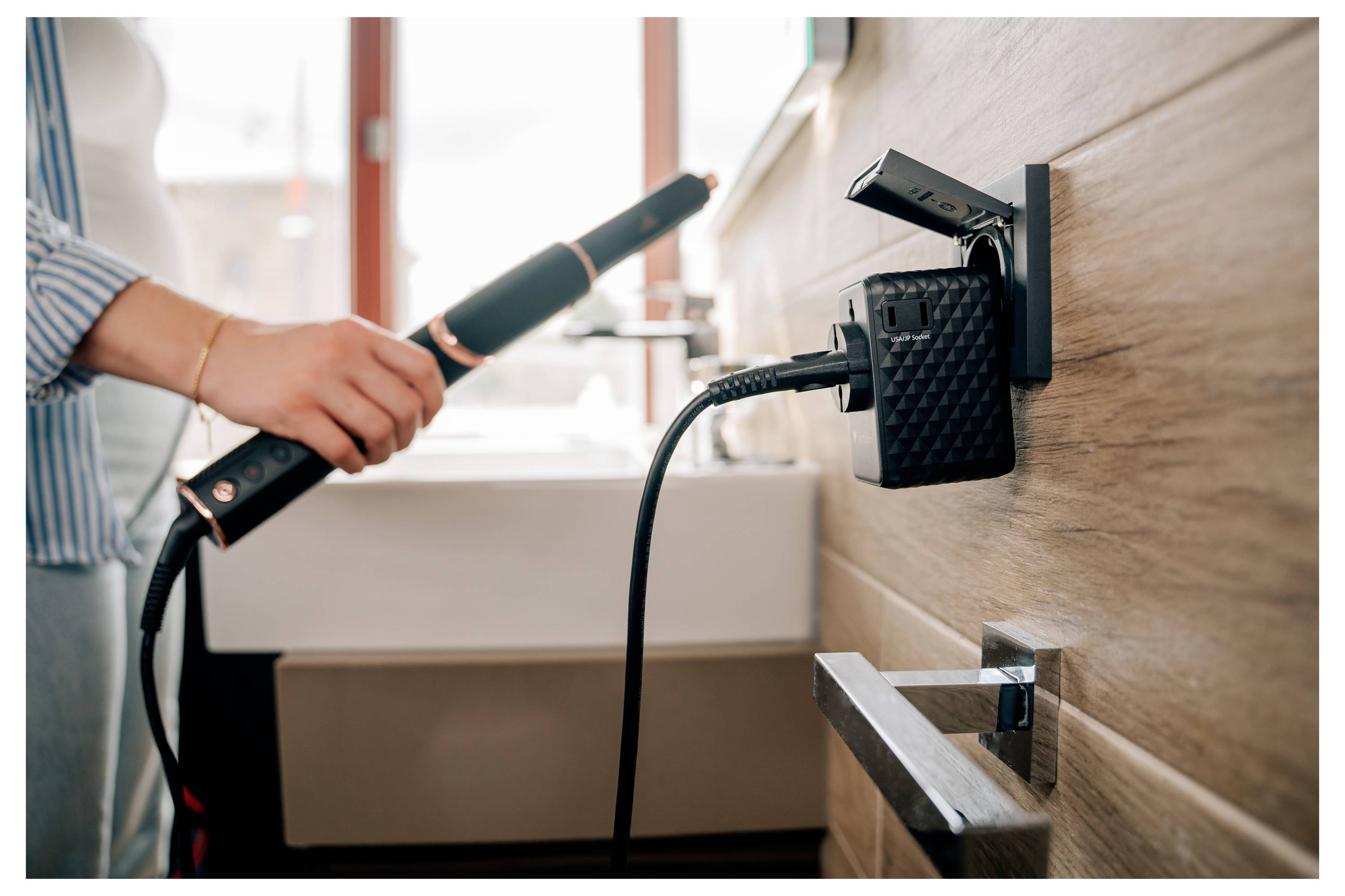Person hält eine elektrische Zahnbürste in der Nähe eines an der Badezimmerwand angebrachten Ladegeräts, wobei die Bürste eingesteckt ist und lädt.