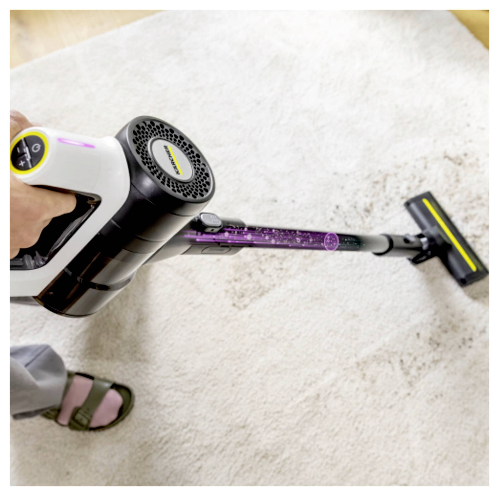 Person mit einem tragbaren, kabellosen Staubsauger, der einen hellfarbigen Teppich absaugt.