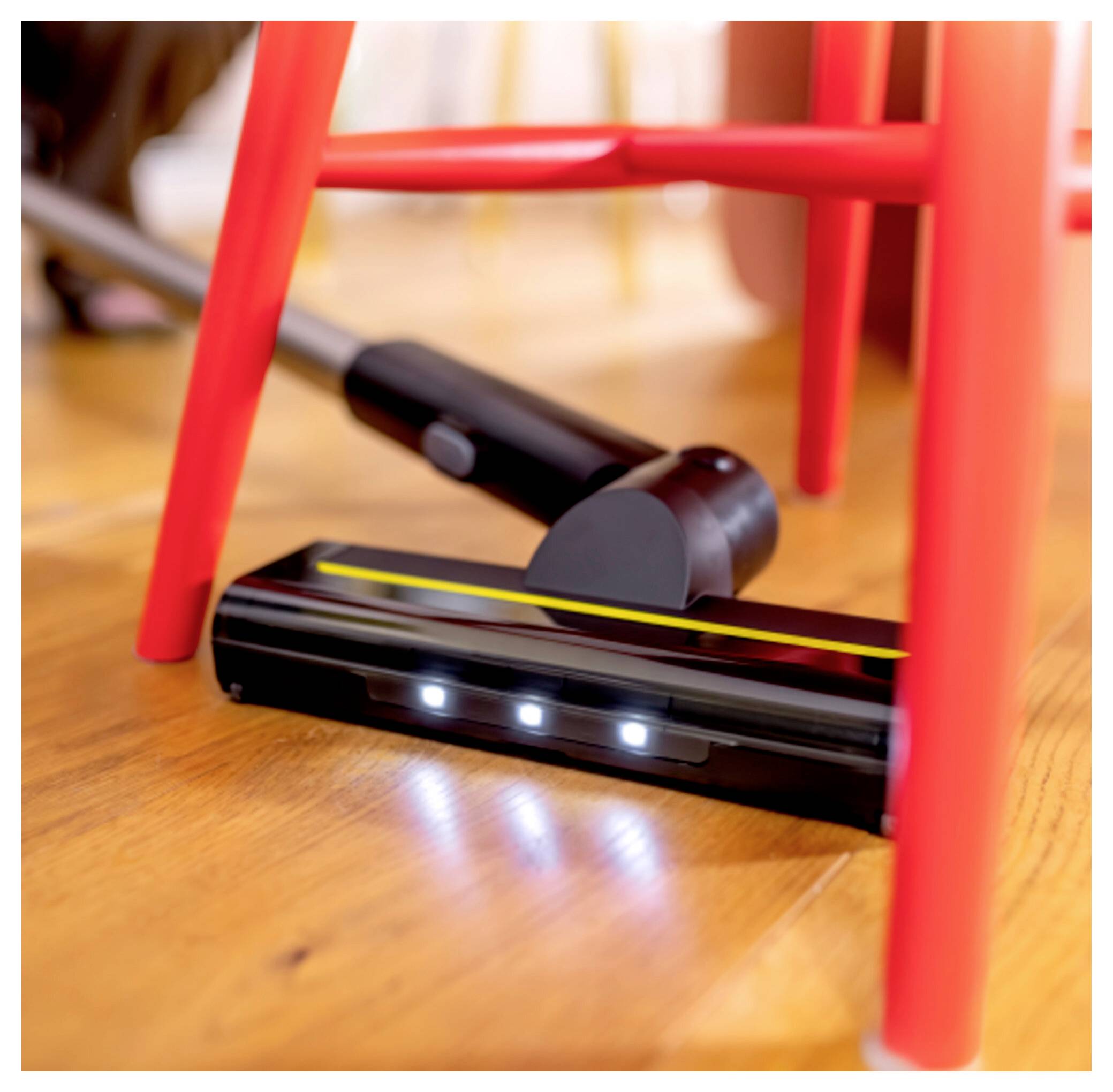 Ein Staubsauger mit LED-Leuchten reinigt einen Hartholzboden, navigiert um rote Stuhlbeine herum und hebt seine Manövrierfähigkeit hervor.