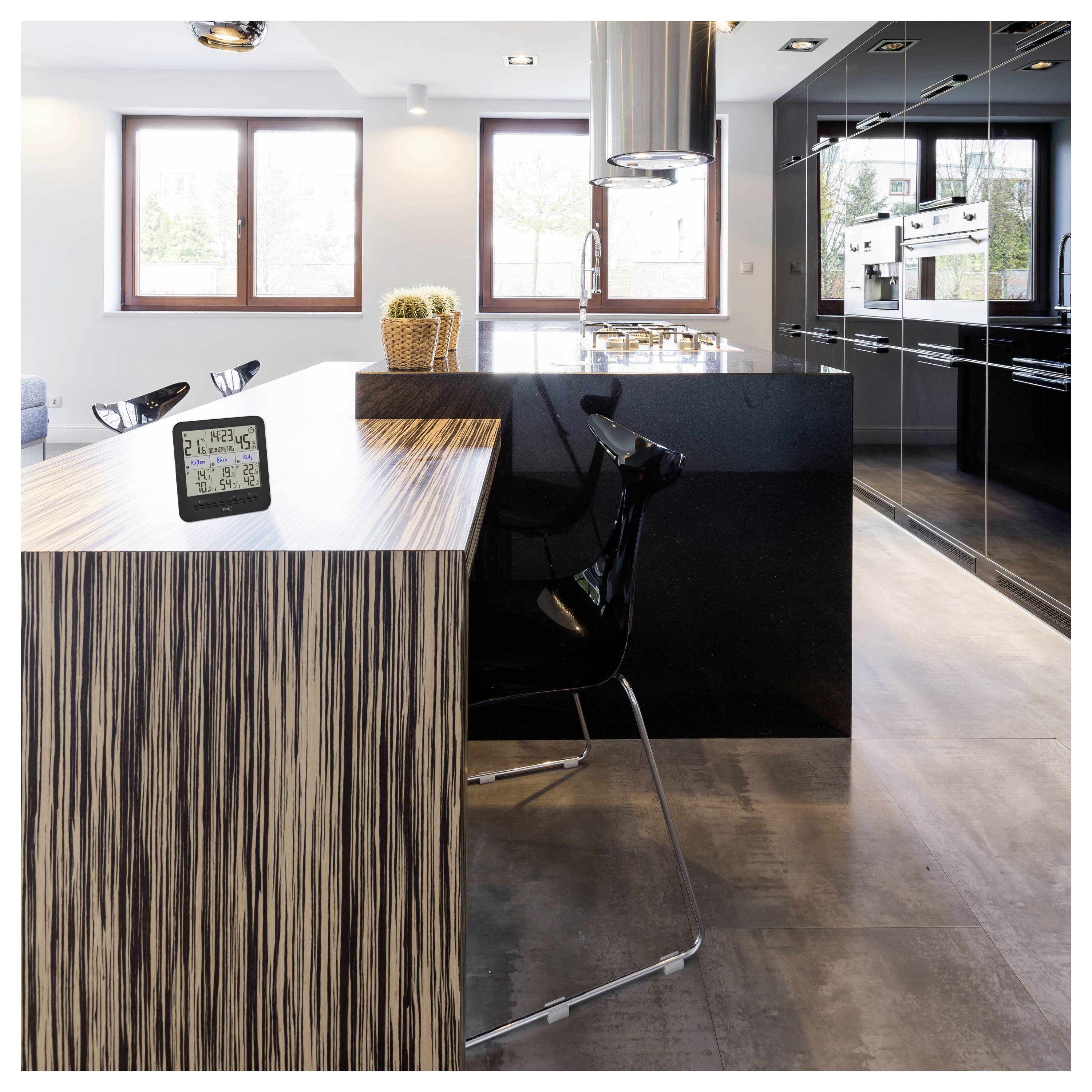 Eine moderne Küche mit einer Kücheninsel im Holzmuster und schwarzem Barhocker. Eine digitale Uhr zeigt Zeit und Datum an. Große Fenster bieten natürliches Licht.