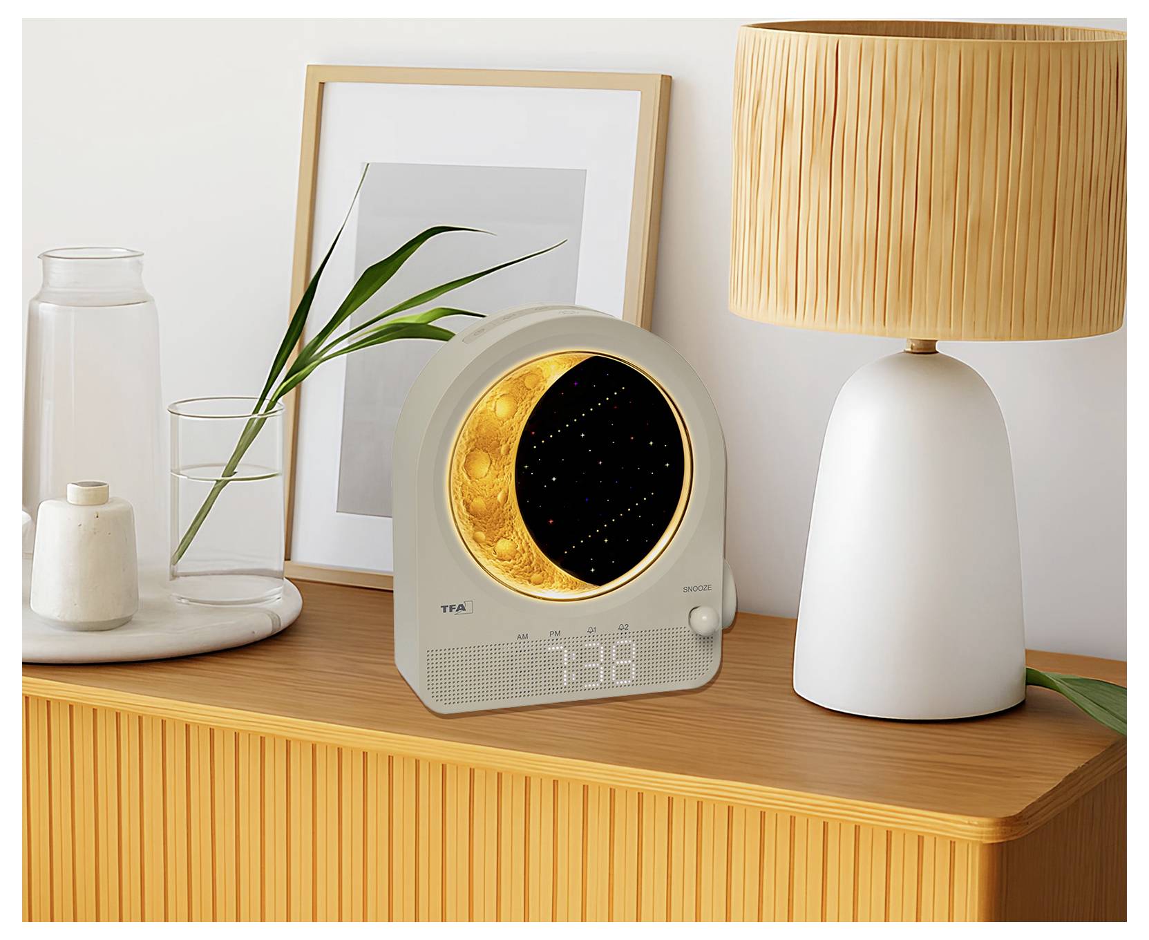 Eine runde digitale Uhr mit einer naturthematischen Nachtlampe auf einem Holzschrank neben einer Lampe und einem gerahmten Bild. Angezeigte Zeit: 7:38.