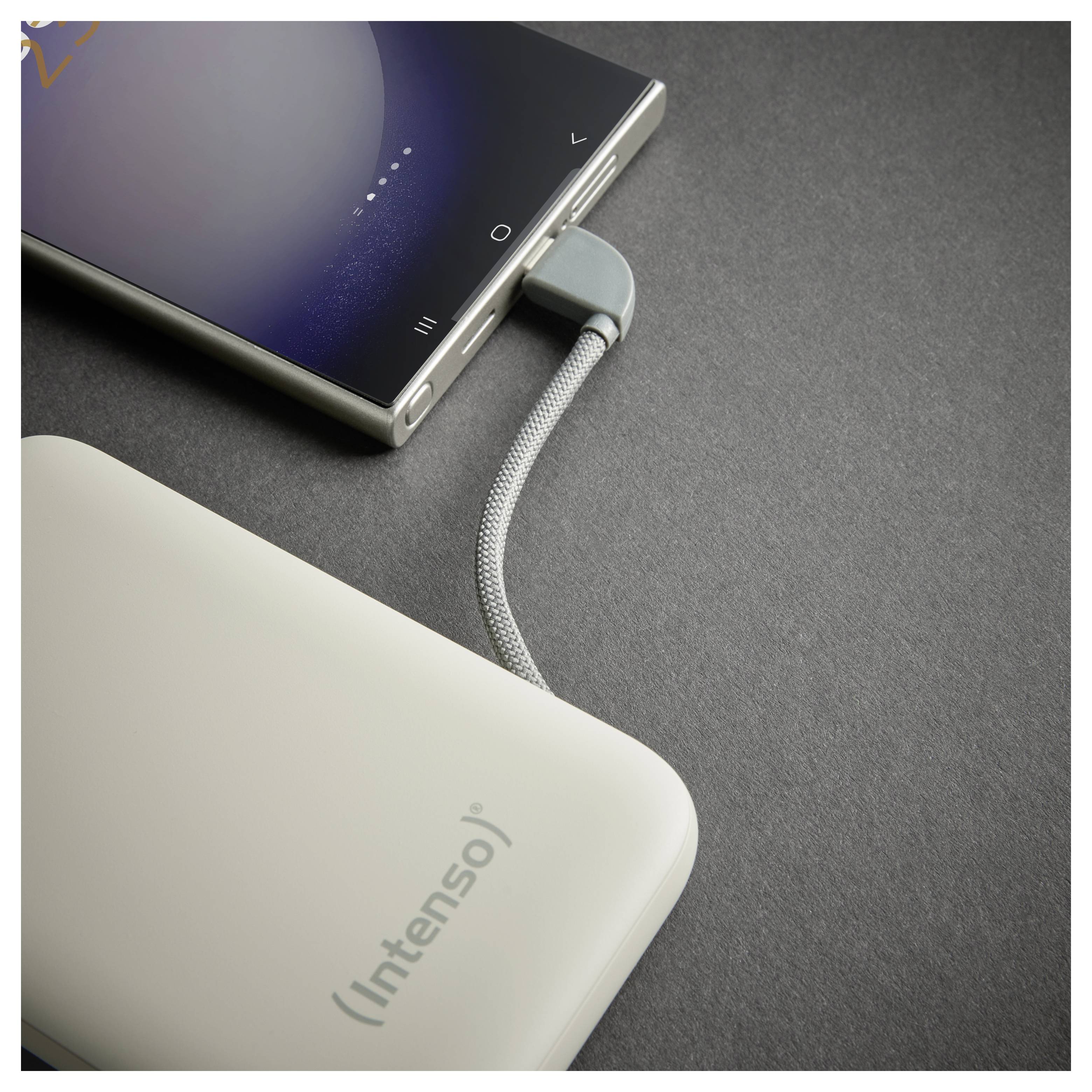 Ein Smartphone, das über ein geflochtenes USB-Kabel mit einer Powerbank verbunden ist, liegt auf einer dunklen Oberfläche; die Powerbank ist mit „Intenso