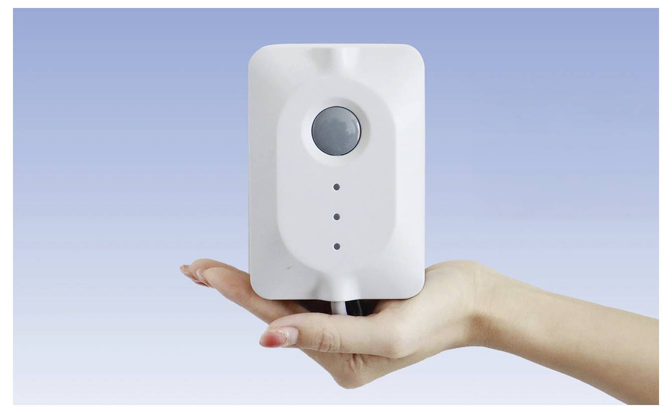 Eine Hand hält ein weißes Gerät mit einem runden Knopf und drei kleinen Anzeigeleuchten vor einem blauen Verlaufshintergrund.