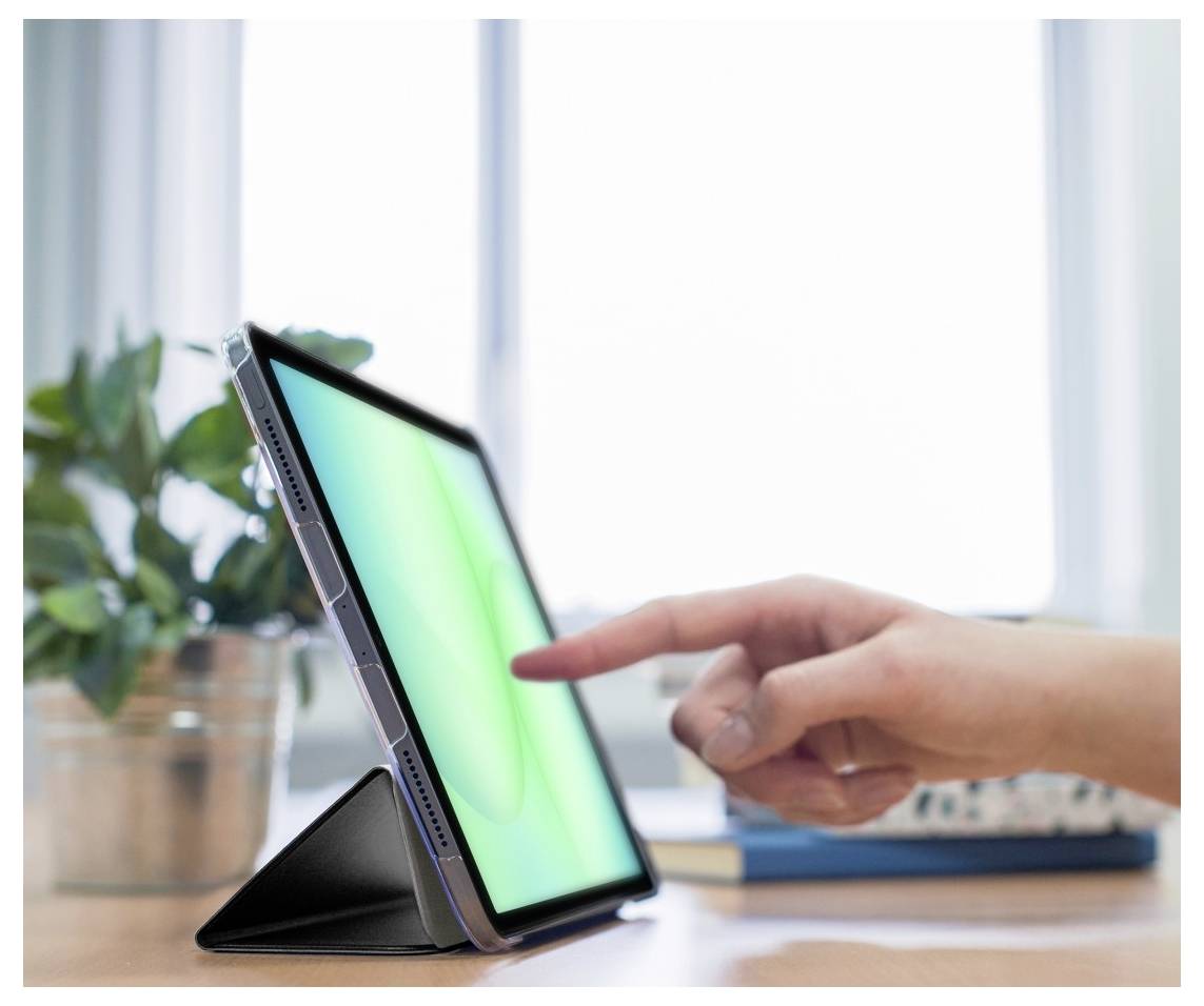 Eine Hand berührt einen Tablet-Bildschirm, der auf einem Ständer ruht. Eine Pflanze und ein Notizbuch sind im unscharfen Hintergrund sichtbar.