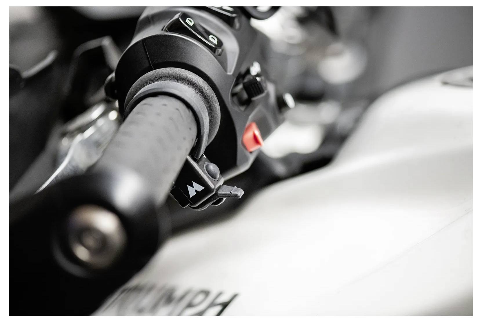 Nahaufnahme eines Motorradlenkers mit dem Griff, einigen Bedienelementen und einem Teil des Benzintanks mit unscharfem Text.