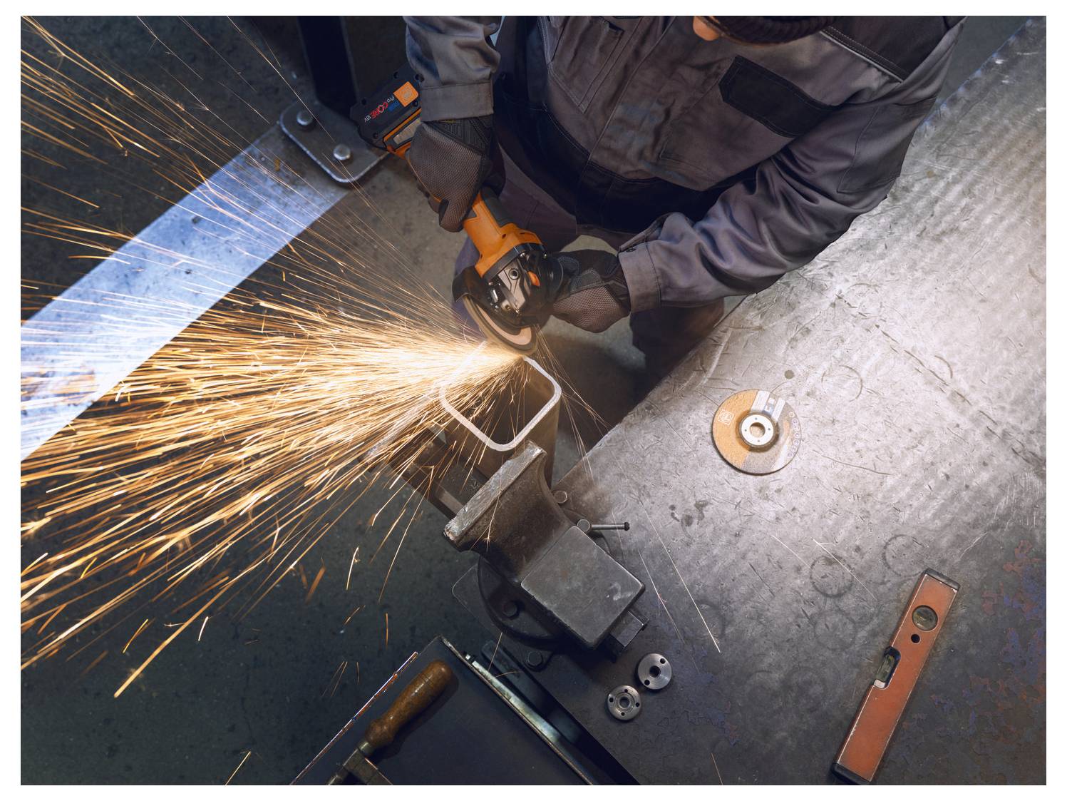 Eine Person nutzt ein Elektrowerkzeug zum Schneiden von Metall und erzeugt dabei helle Funken. Die Szene spielt sich in einer Werkstatt ab, in der verschiedene Werkzeuge und Ausrüstungen sichtbar sind.