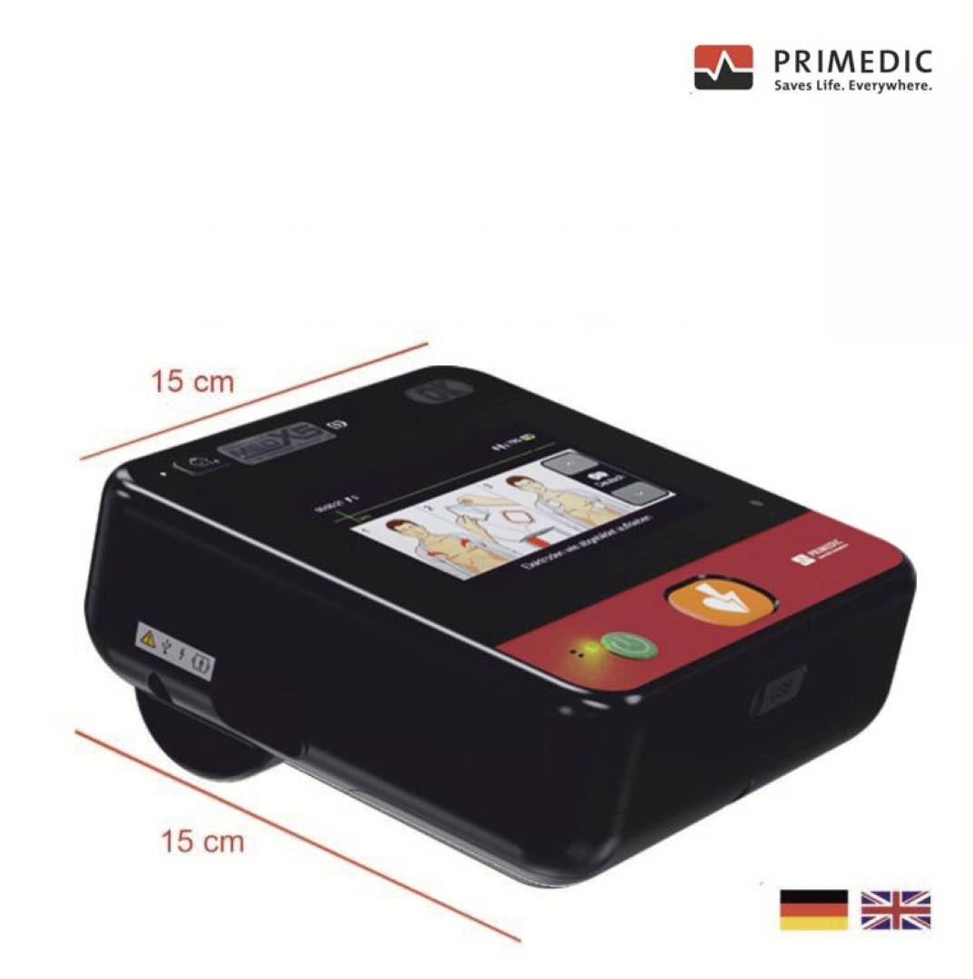 Das Bild zeigt einen kompakten, schwarzen Primedic-Defibrillator mit den Abmessungen 15x15 cm, mit einem Bildschirm und Bedientasten sowie britischen und deutschen Flaggen.