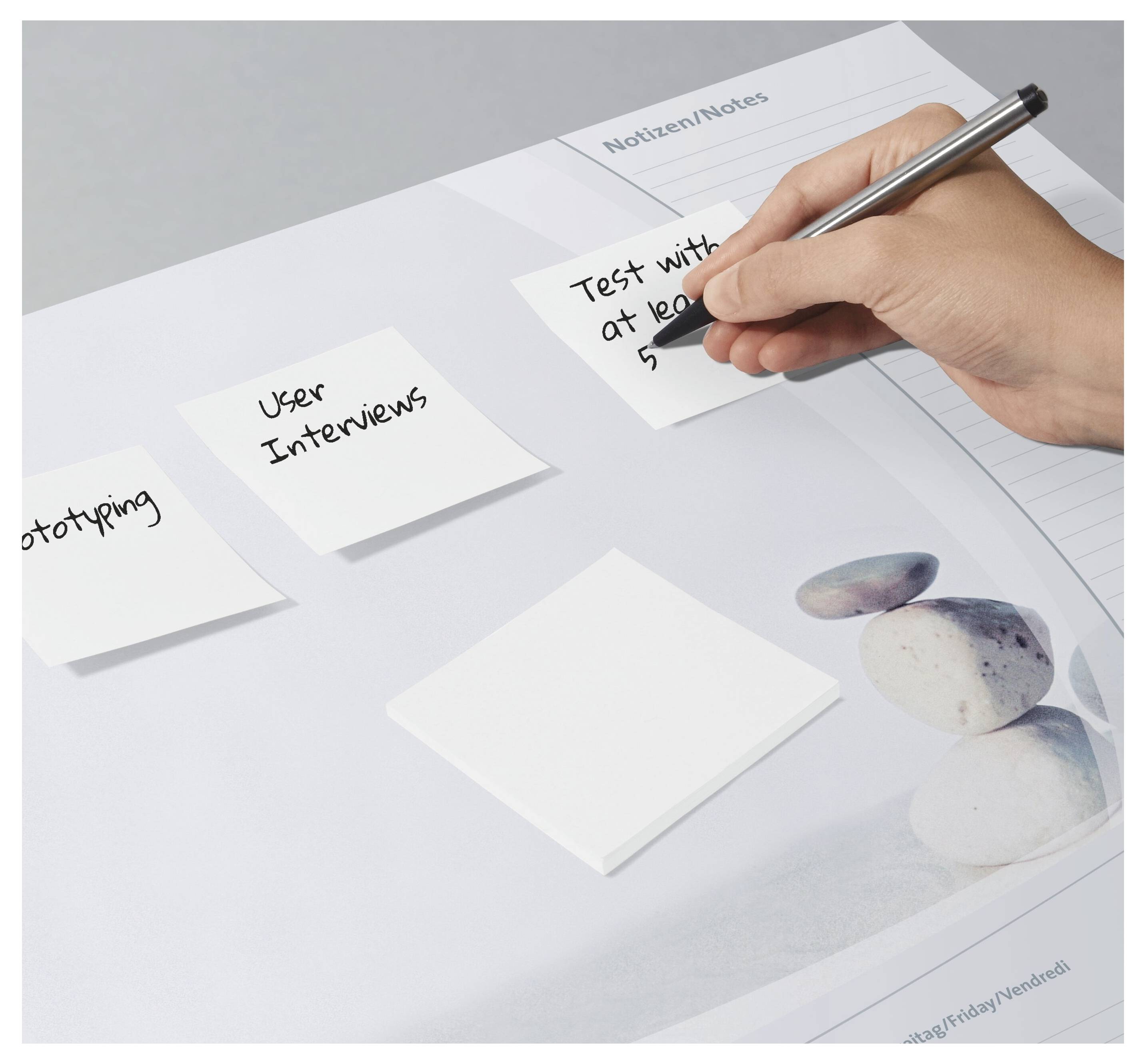 Eine Hand schreibt auf einen Klebezettel mit der Aufschrift „Test mit mindestens 5