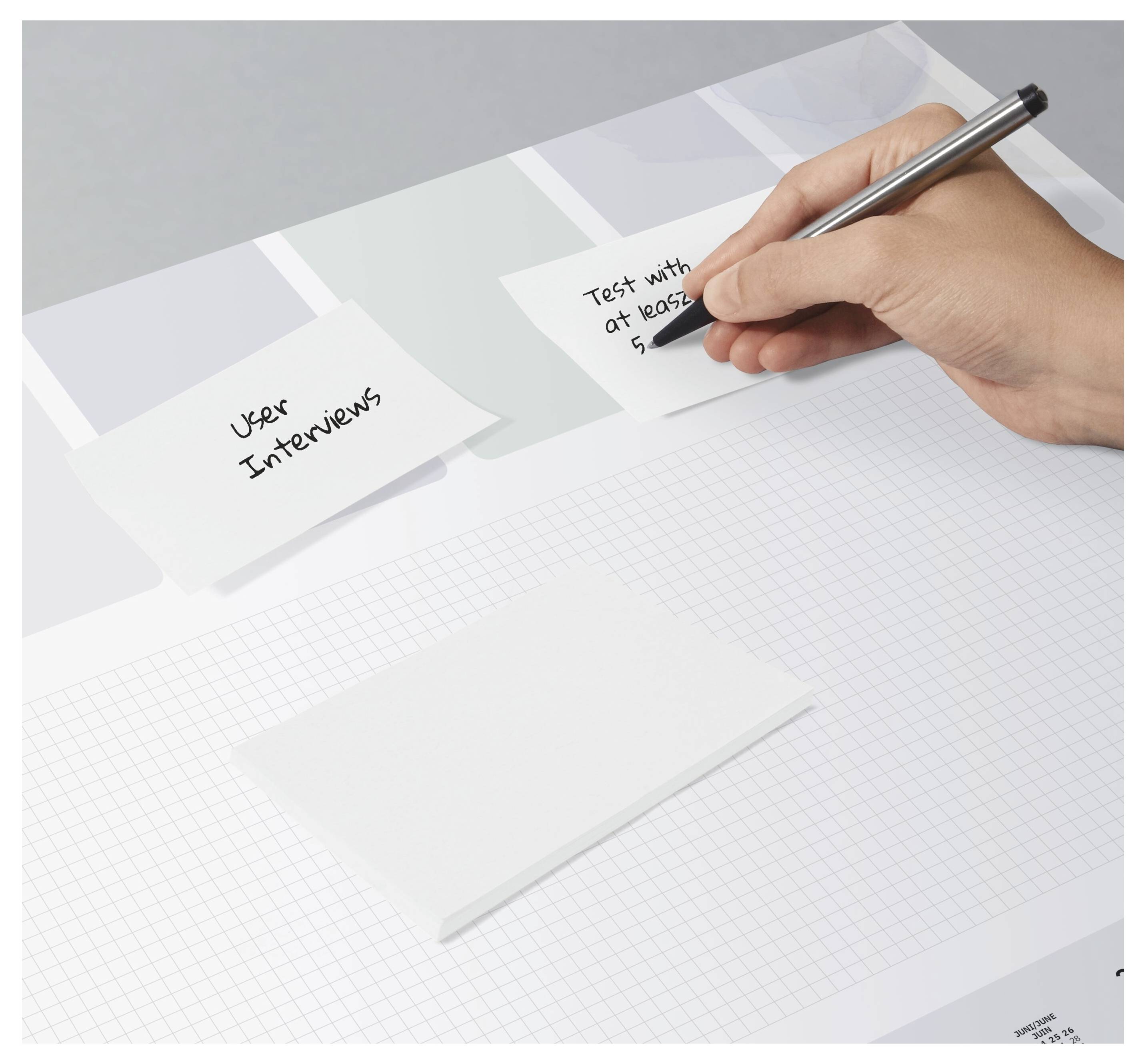 Ein Mensch schreibt mit einem Stift in der Hand auf einen Klebezettel. Ein anderer Zettel ist mit „Benutzerinterviews