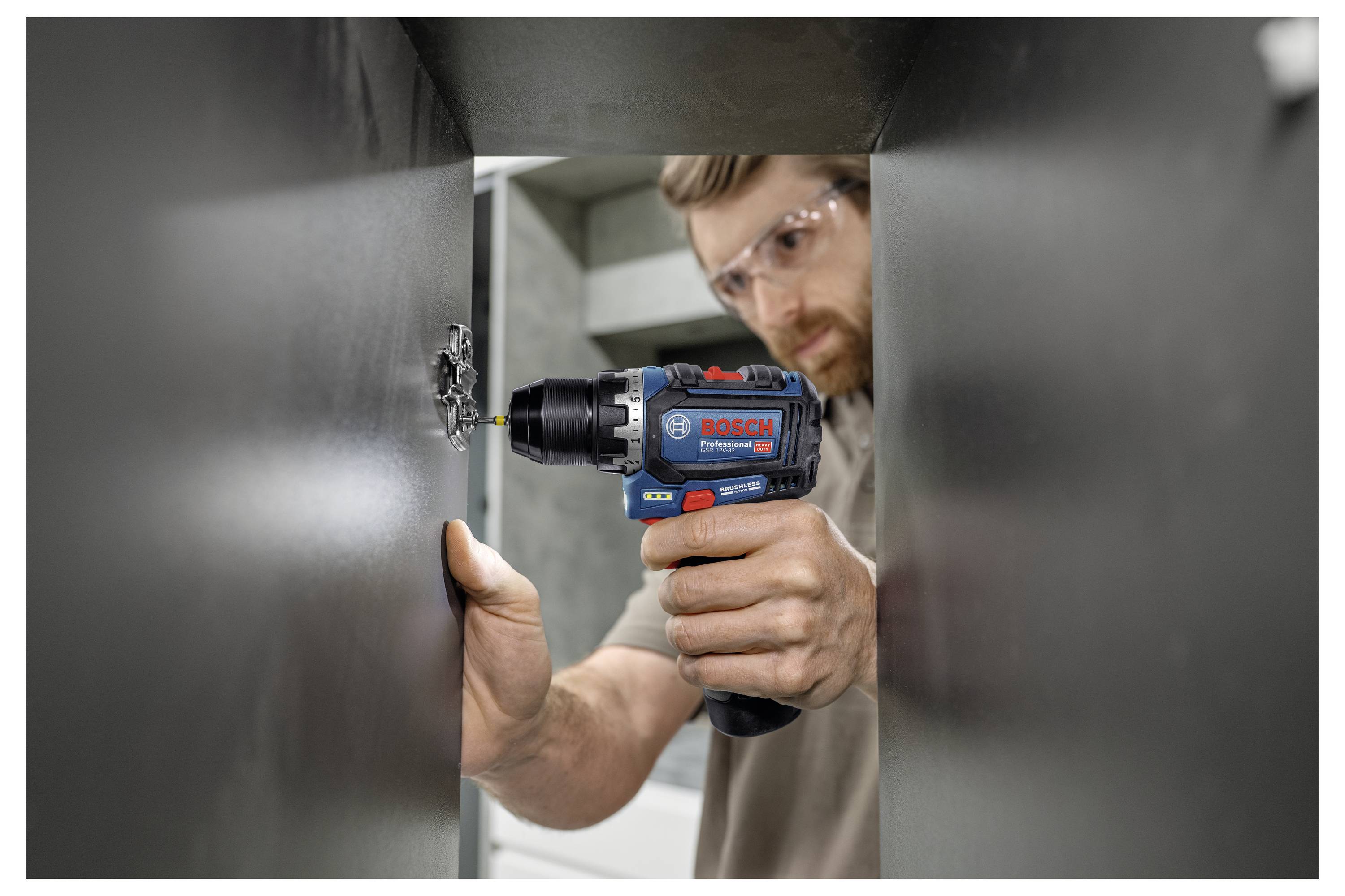 Eine Person, die eine Schutzbrille trägt, verwendet einen kabellosen Bosch-Bohrer, um eine Halterung in einem Metallgehäuse zu befestigen.