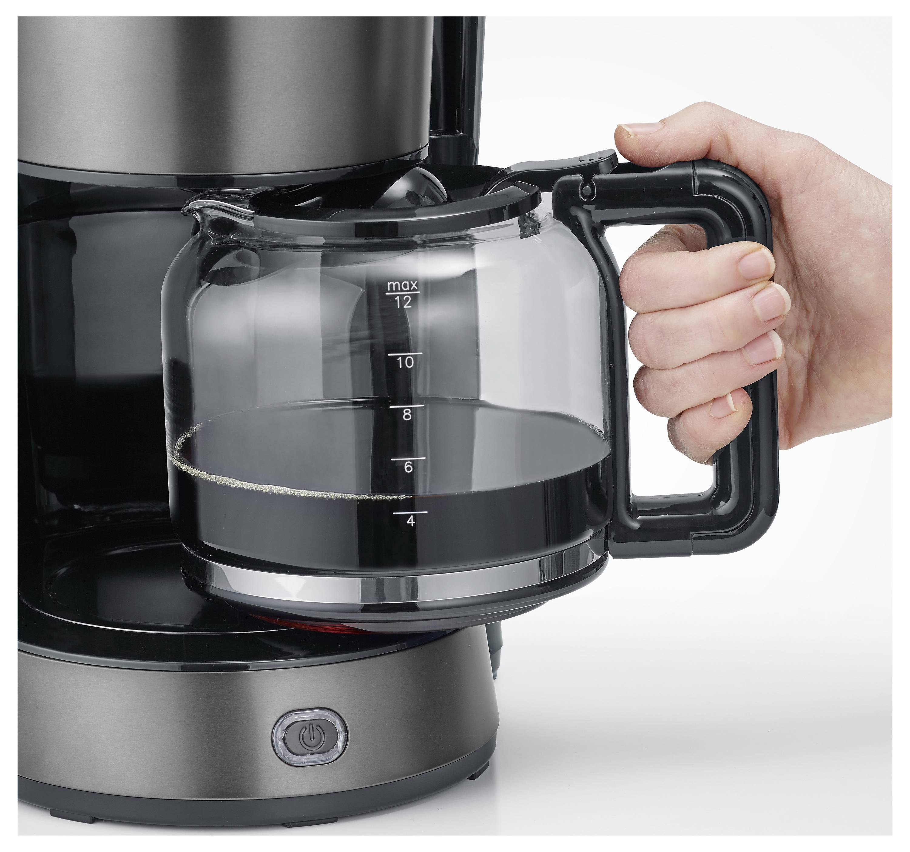 Eine Hand hält eine Glaskaffeekanne, zur Hälfte mit Kaffee gefüllt, vor einer Kaffeemaschine. Das 