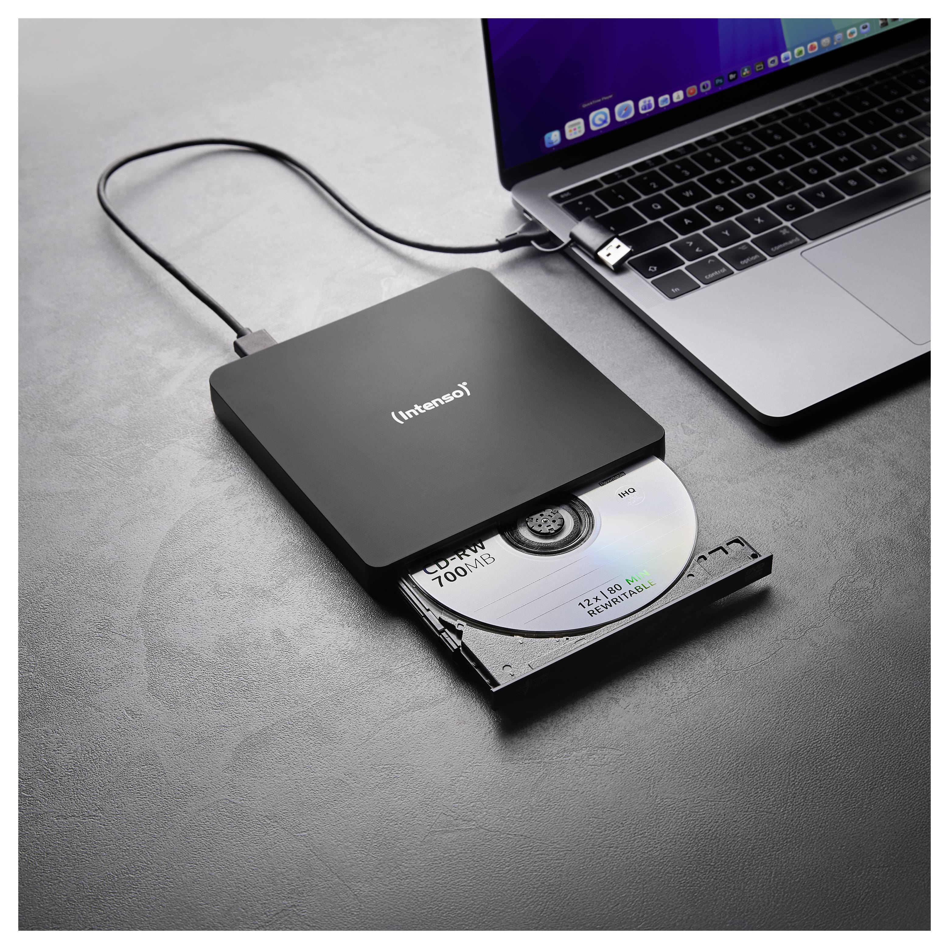 Ein schwarzes externes CD/DVD-Laufwerk, das mit einem offenen Laptop verbunden ist, zeigt eine teilweise ausgefahrene Disc. Der Laptop zeigt einen unscharfen Bildschirm.