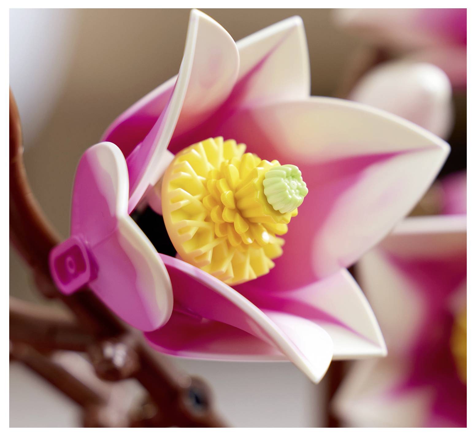 Eine Nahaufnahme einer rosa und weißen Kunststoffspielzeugblume mit gelbem und grünem Zentrum, befestigt an einem braunen Stiel.