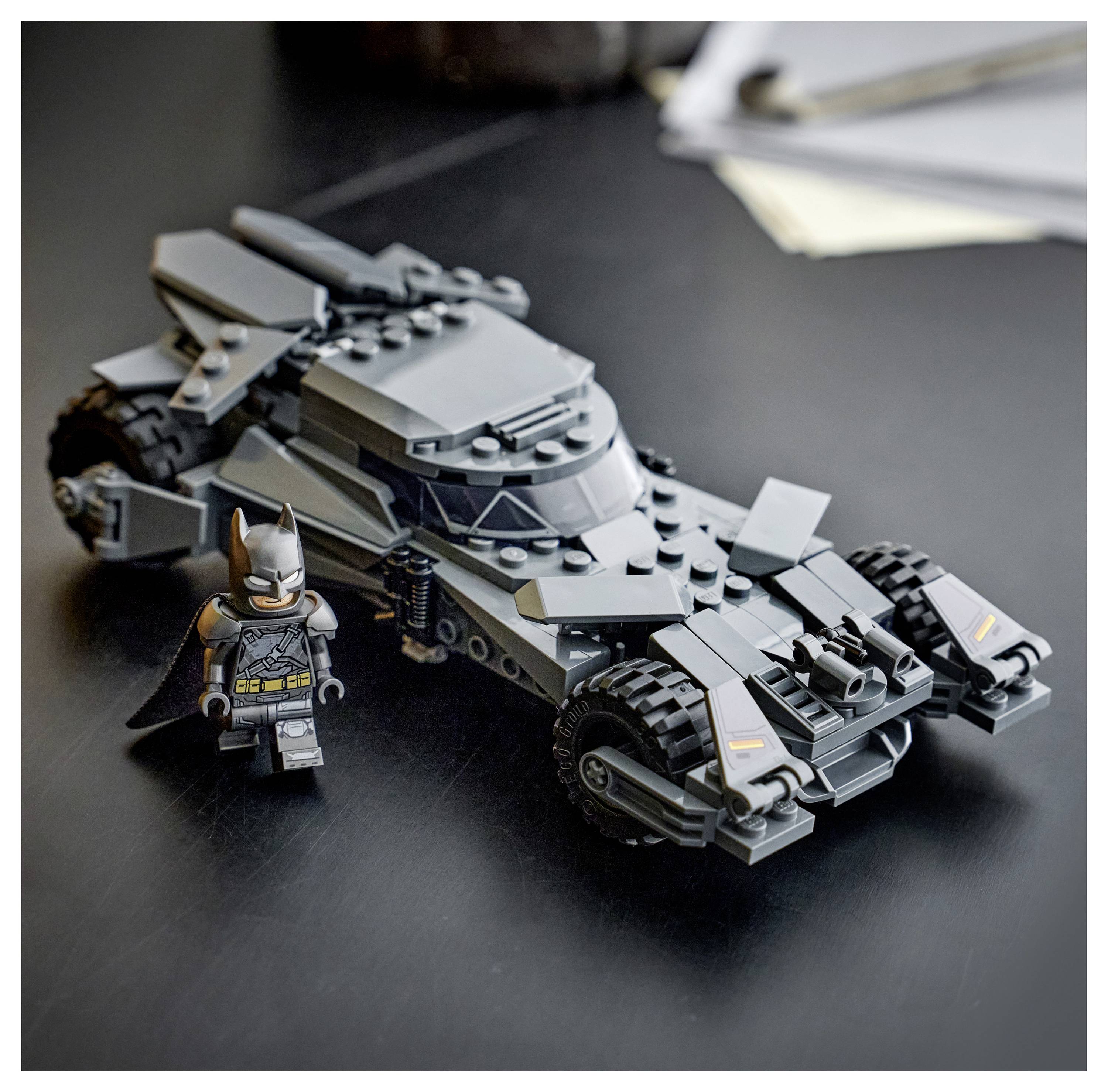 LEGO-Modell eines schwarzen Batmobile mit einer Batman-Figur, auf einem dunklen Tisch neben Papieren platziert. Das Batmobile hat kantige Designmerkmale.