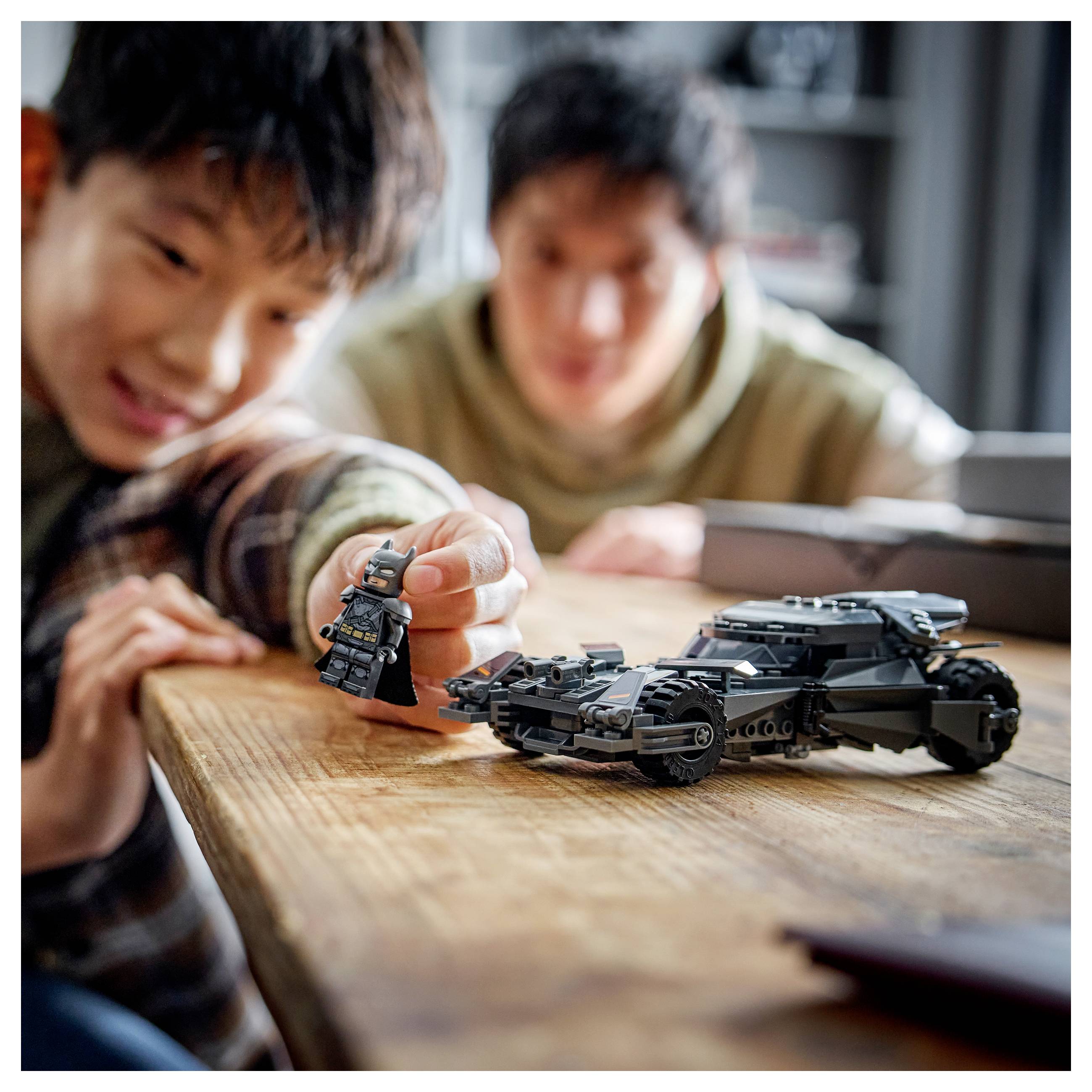 Zwei Personen spielen mit einem kleinen Spielzeugauto und einer Figur auf einem Holztisch und wirken dabei konzentriert und engagiert.
