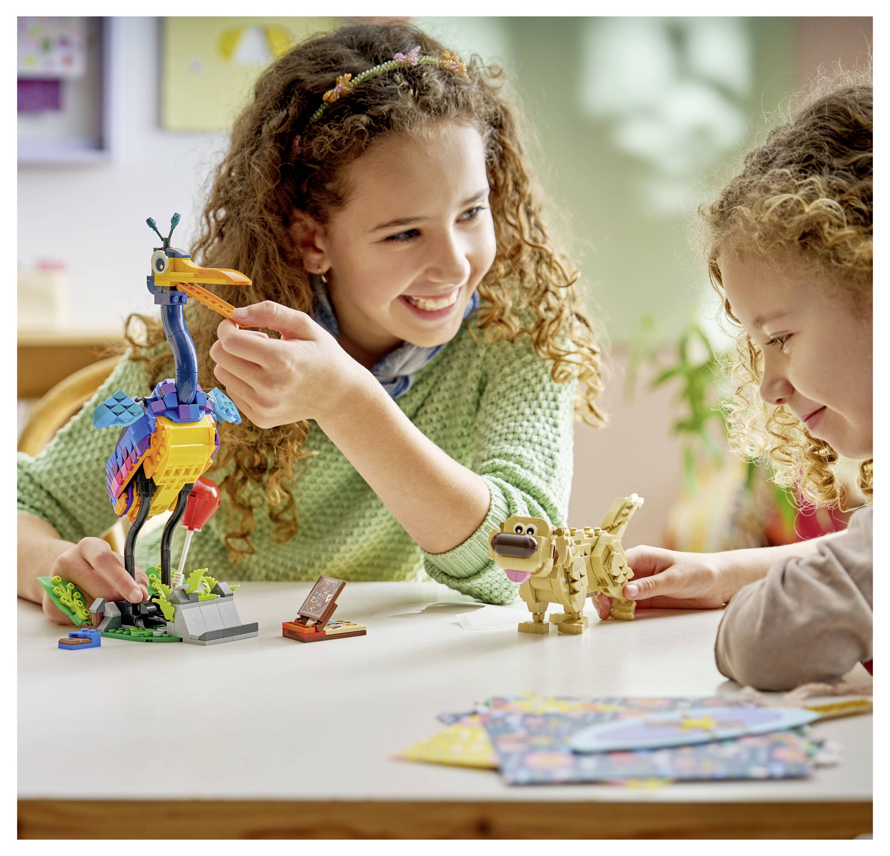 Kinder spielen mit bunten Bausteinen und erschaffen einen Vogel und einen Dinosaurier, lächeln und sind bei fantasievollem Spiel an einem Tisch vertieft.