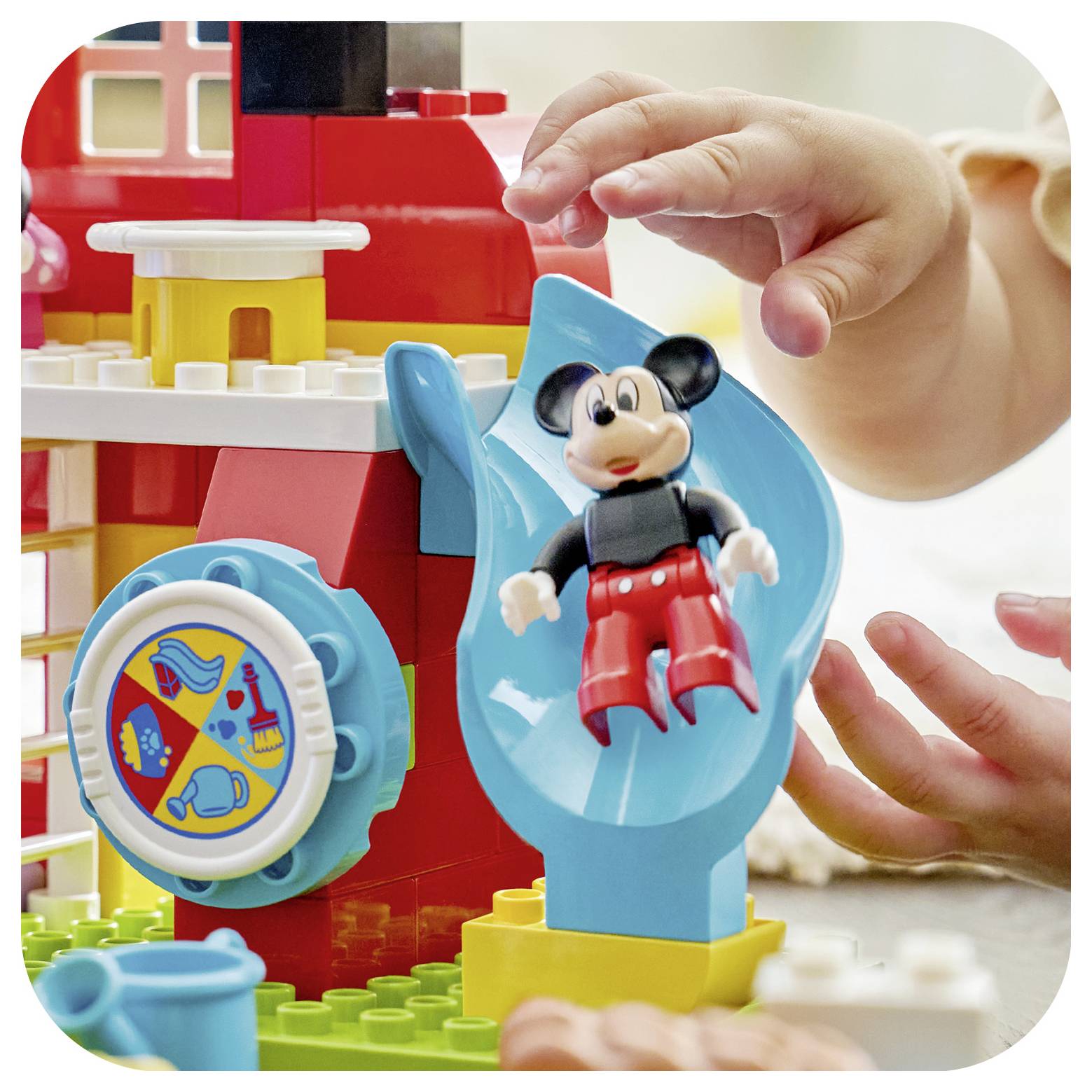 Ein Kind greift danach, um mit einer Rutsche zu spielen, auf der sich eine kleine Figur auf einer bunten Bausteinstruktur befindet.