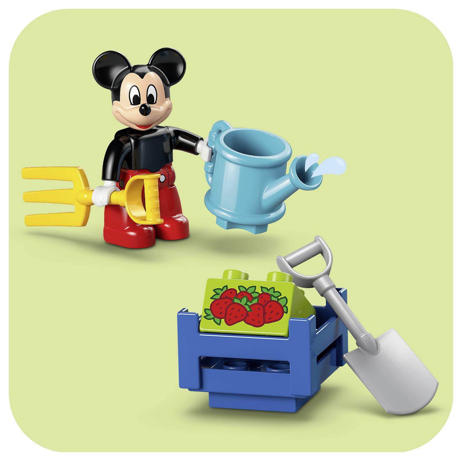 LEGO-Figur der Maus Micky hält eine Gießkanne und eine Heugabel und steht neben einer Kiste mit Erdbeeren und einer Schaufel auf grünem Hintergrund.