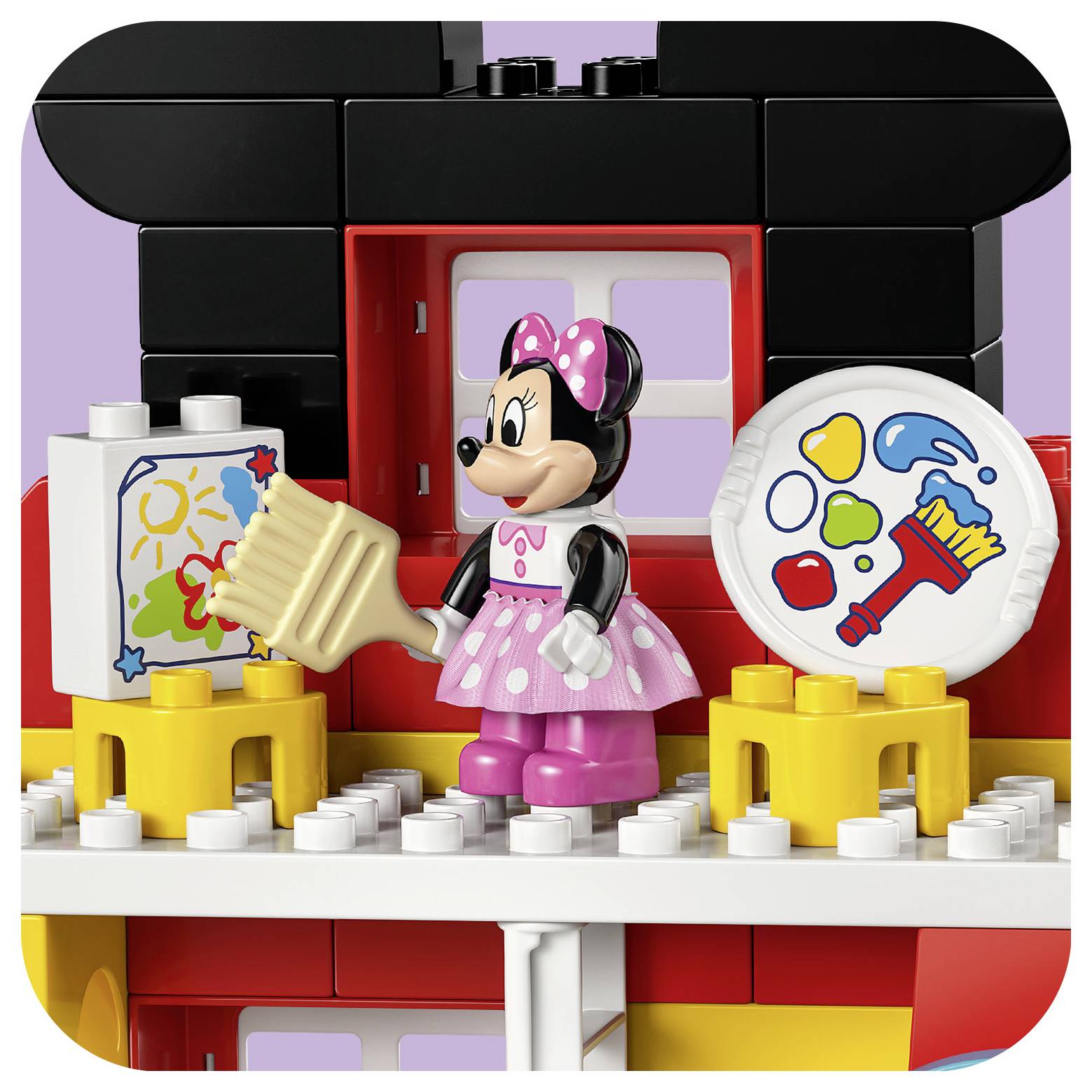 Eine Spielzeugfigur einer Zeichentrickmaus, die in Rosa gekleidet ist, steht auf einem farbenfrohen Gebäudeset mit Kunstbedarf, einschließlich eines Pinsels und einer Palette.