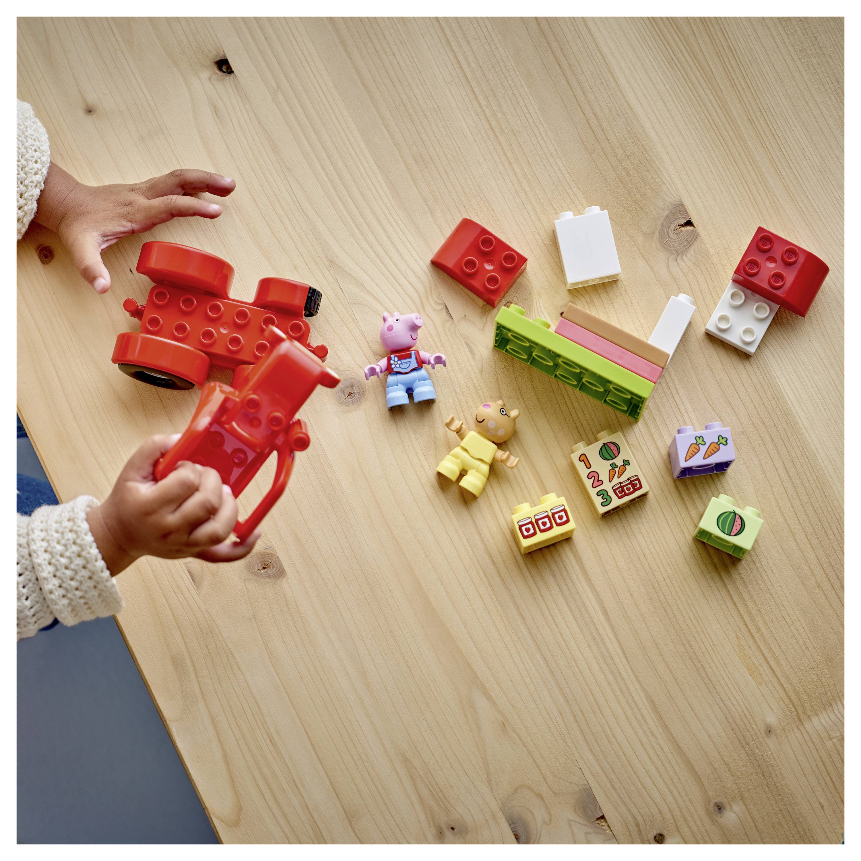 Ein Kind spielt mit verstreuten bunten Kunststoffblöcken und Spielfiguren auf einem Holztisch und ordnet die Teile an und interagiert mit ihnen.