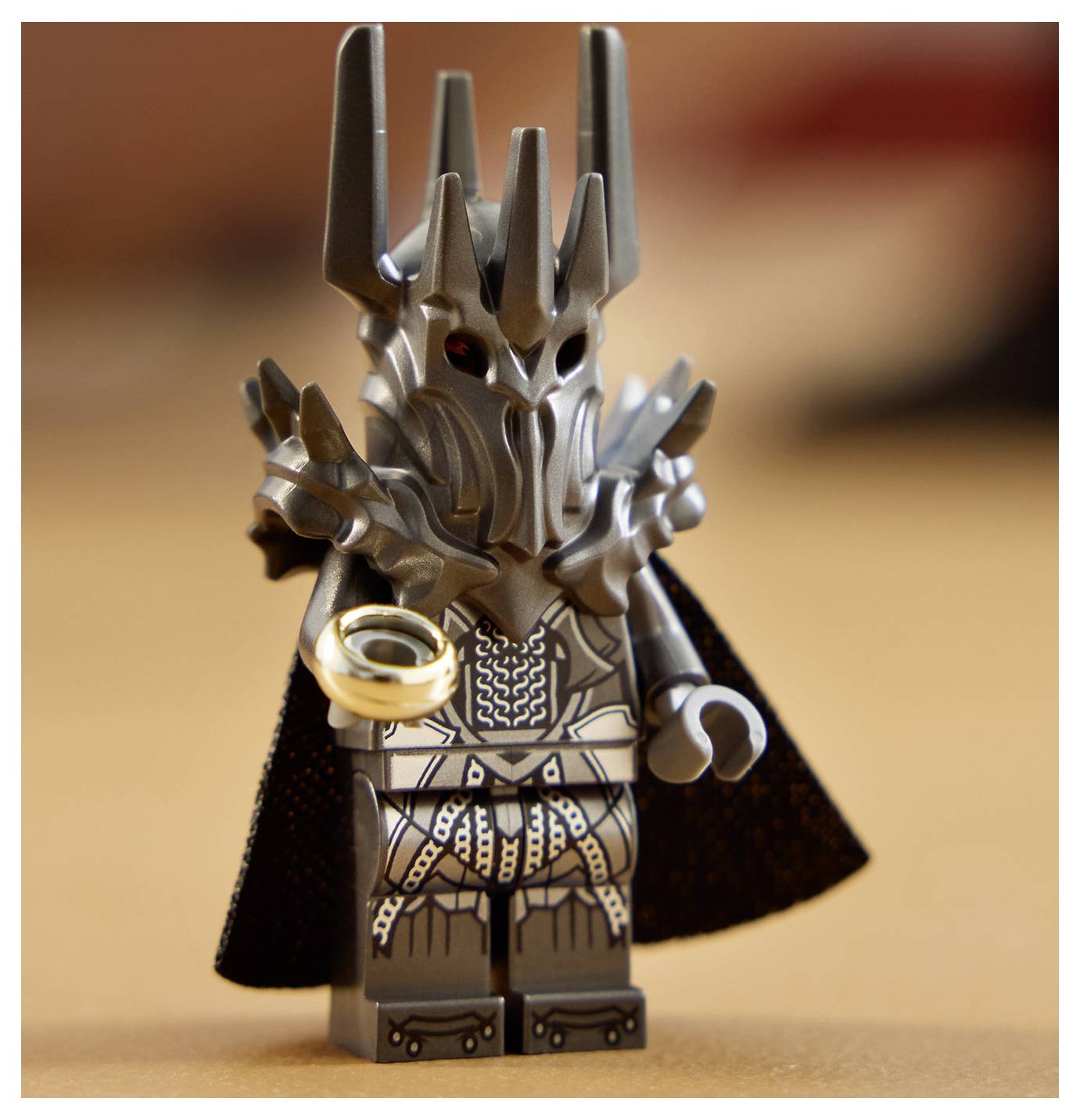 Eine Spielzeugfigur eines dunkel gepanzerten Charakters mit einem bedrohlich wirkenden Helm, der einen goldenen Ring hält, vor einem unscharfen Hintergrund.