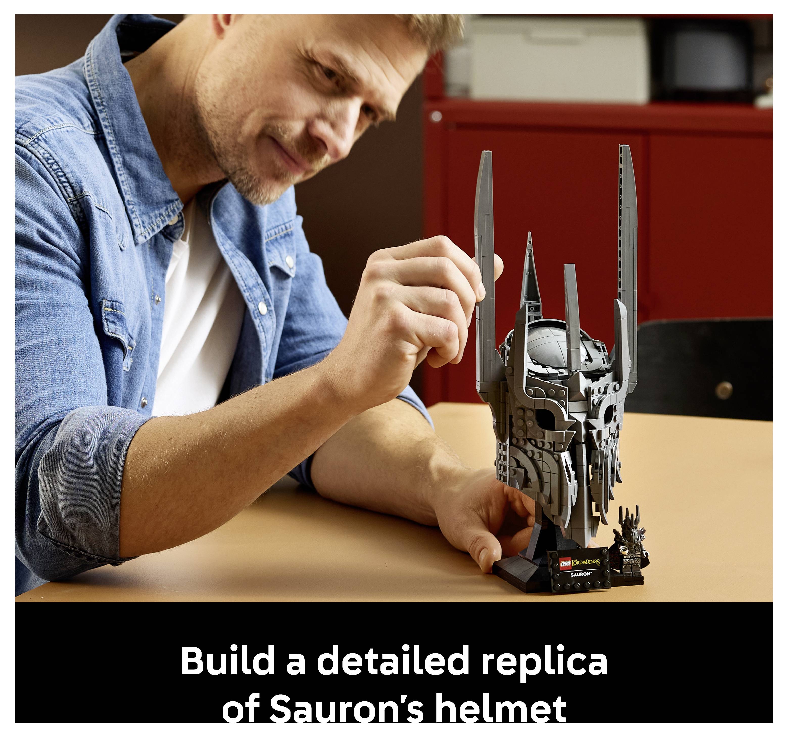 Ein Mann, der an einem Tisch eine detaillierte LEGO-Nachbildung von Saurons Helm zusammenbaut. Die Bildunterschrift lautet: „Bauen Sie eine detaillierte Nachbildung von Saurons Helm.