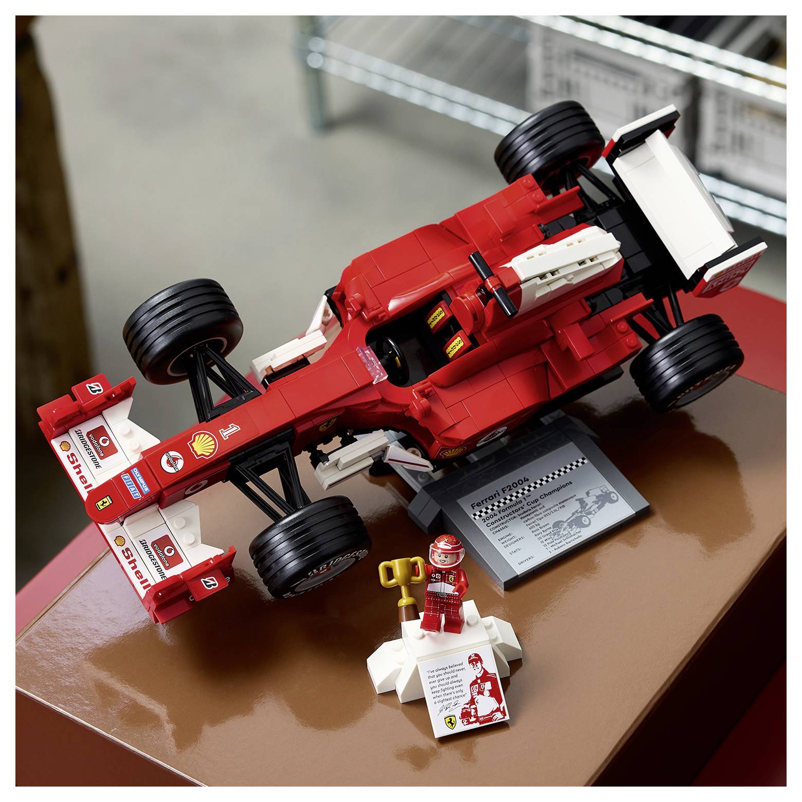Ein detailliertes rot-weißes LEGO-Modell eines Rennwagens auf einem Display mit einer kleinen Figur und einer Plakette.