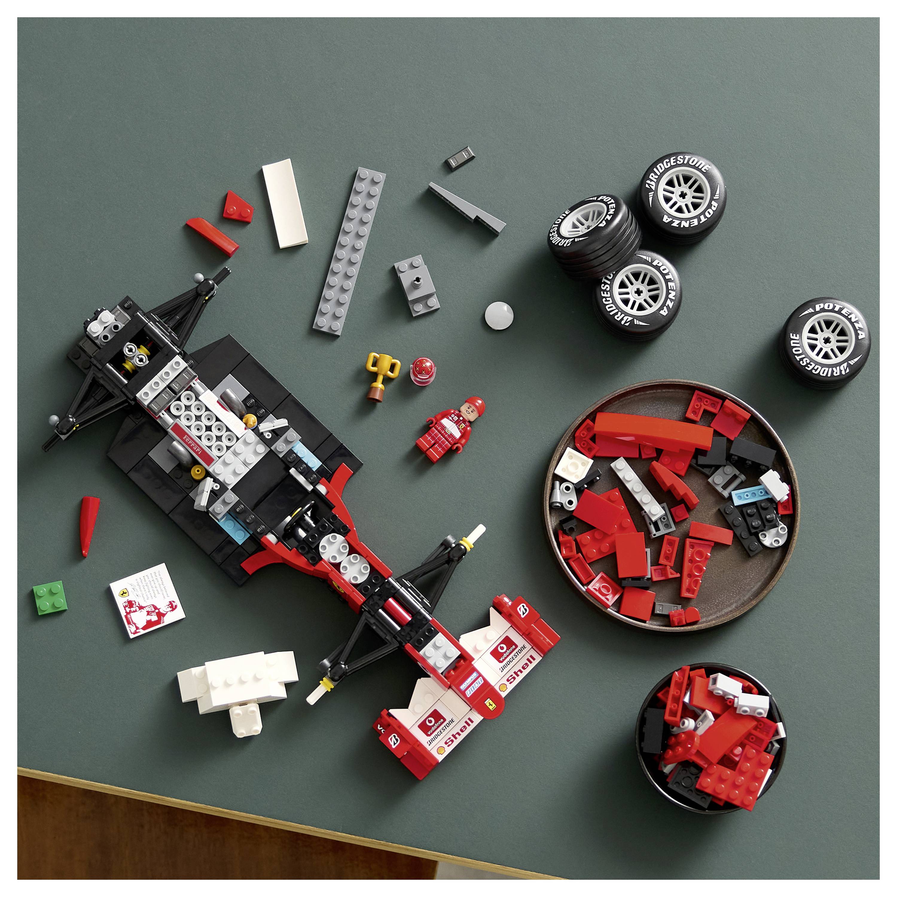 Ein zerlegtes rot-schwarzes Spielzeugrennauto mit Teilen und vier Reifen, die auf einer dunklen Oberfläche angeordnet sind und verschiedene Autoteile zeigen.