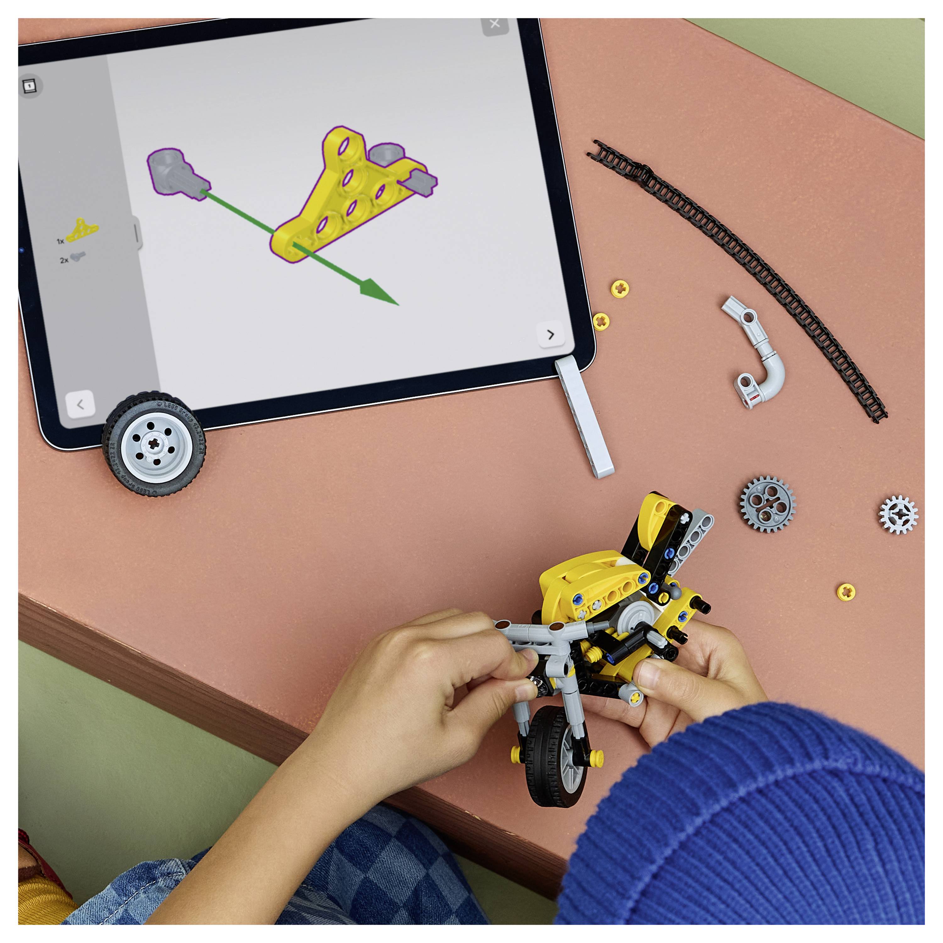 Ein Kind baut ein gelbes robotisches Spielzeug-Motorrad auf einem Tisch zusammen und folgt dabei den Anweisungen auf einem Tablet.