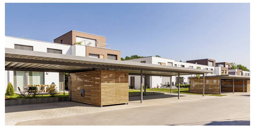 Moderner Mehrfamilienhauskomplex mit niedriger Bebauung, holzverkleideter Eingangsüberdachung, Balkonen und einem sonnigen gepflasterten Innenhof