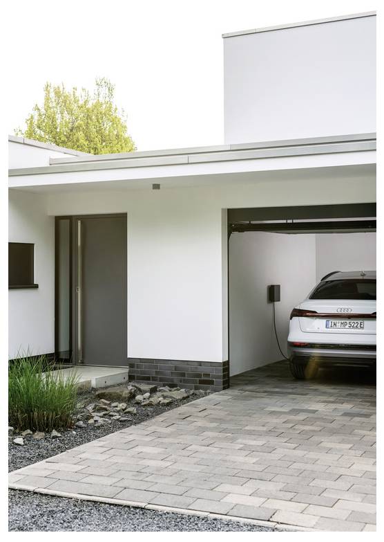 Modernes Außendesign des Weißen Hauses mit einer Auffahrt, die zu einer Garage führt, in der ein silberner Audi drinnen zum Aufladen geparkt ist.