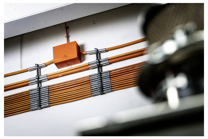 Orangefarbene elektrische Anschlussdose mit mehreren orangefarbenen Kabeln, die ordentlich entlang einer Wand verlegt sind und auf eine industrielle Verdrahtung oder Netzwerkinfrastruktur hindeuten.