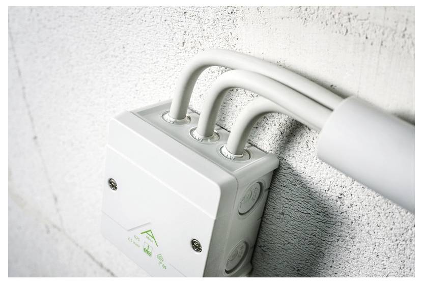 Weiße elektrische Verteilerdose, die auf einer strukturierten Wand montiert ist, mit drei weißen Rohren, die von oben eindringen.