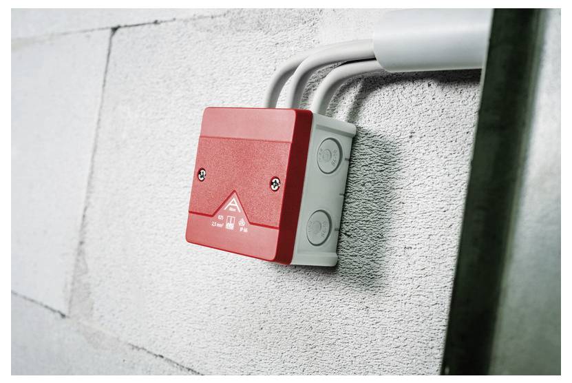 Rotes, wandmontiertes Notfall-Alarmkästchen mit angeschlossenem Rohrsystem auf einer strukturierten Wand.