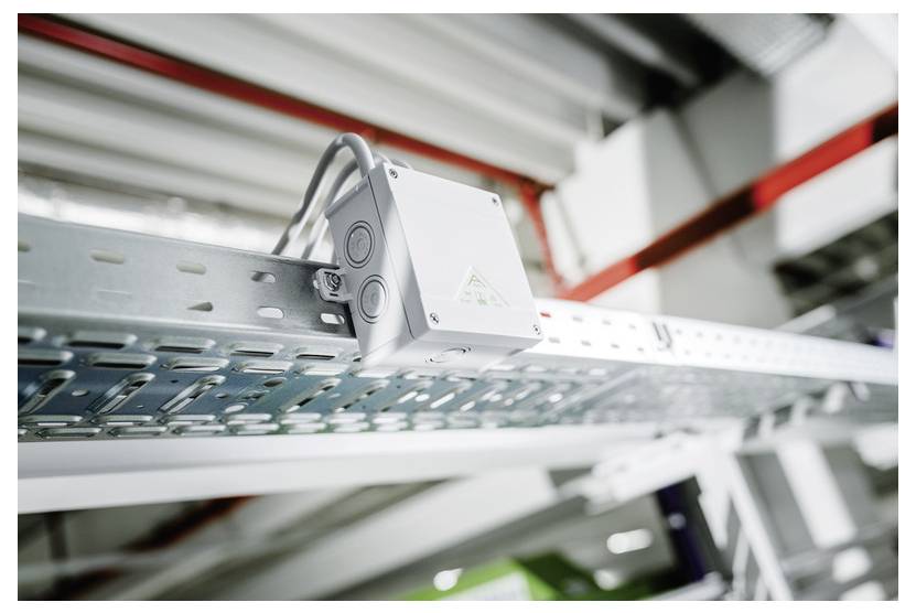 Industrielle elektrische Anschlussdose, die auf einem Metallkabelwagen in einer Fabrikumgebung montiert ist, mit angebrachten Rohrleitungsrohren.