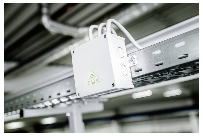 Weißes Netzwerkgerät, das auf einer Metallschiene in einer Versorgungsdecke montiert ist, mit angeschlossenen Kabeln.