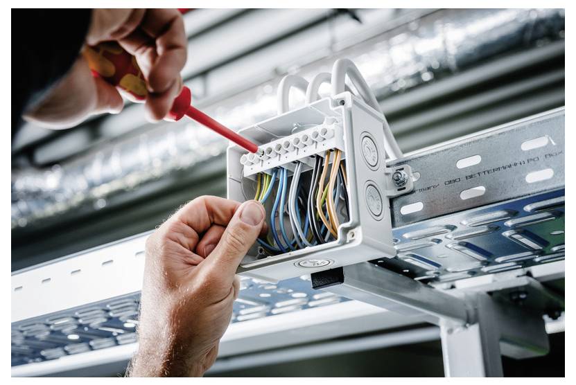 Techniker verdrahtet eine offene elektrische Verteilerdose auf einer Metallkabelwanne und verwendet einen Schraubenzieher, um Anschlussverbindungen festzuziehen.