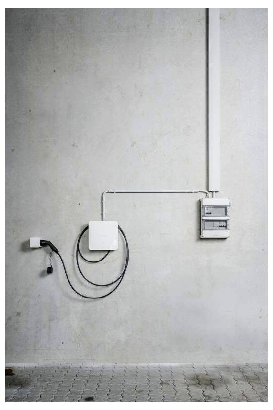 Eine elektrische Wandinstallation mit Kabelkanal, Abzweigdose, aufgewickeltem Kabel und Schutzschaltertafel an einer ebenen Betonwand.