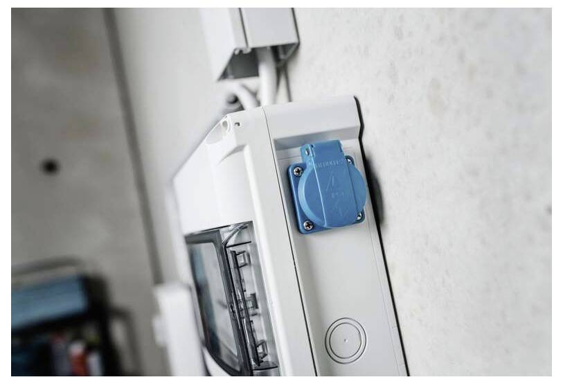 Nahaufnahme einer an der Wand montierten elektrischen Schalttafel mit einer blauen Steckdosenabdeckung an der Vorderseite.